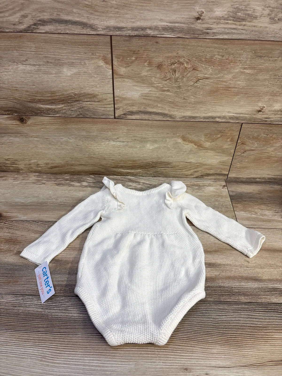 Flat lay of white baby bubble romper with sweater knit, ruffle shoulders and long sleeves, size 9M, on wood floor