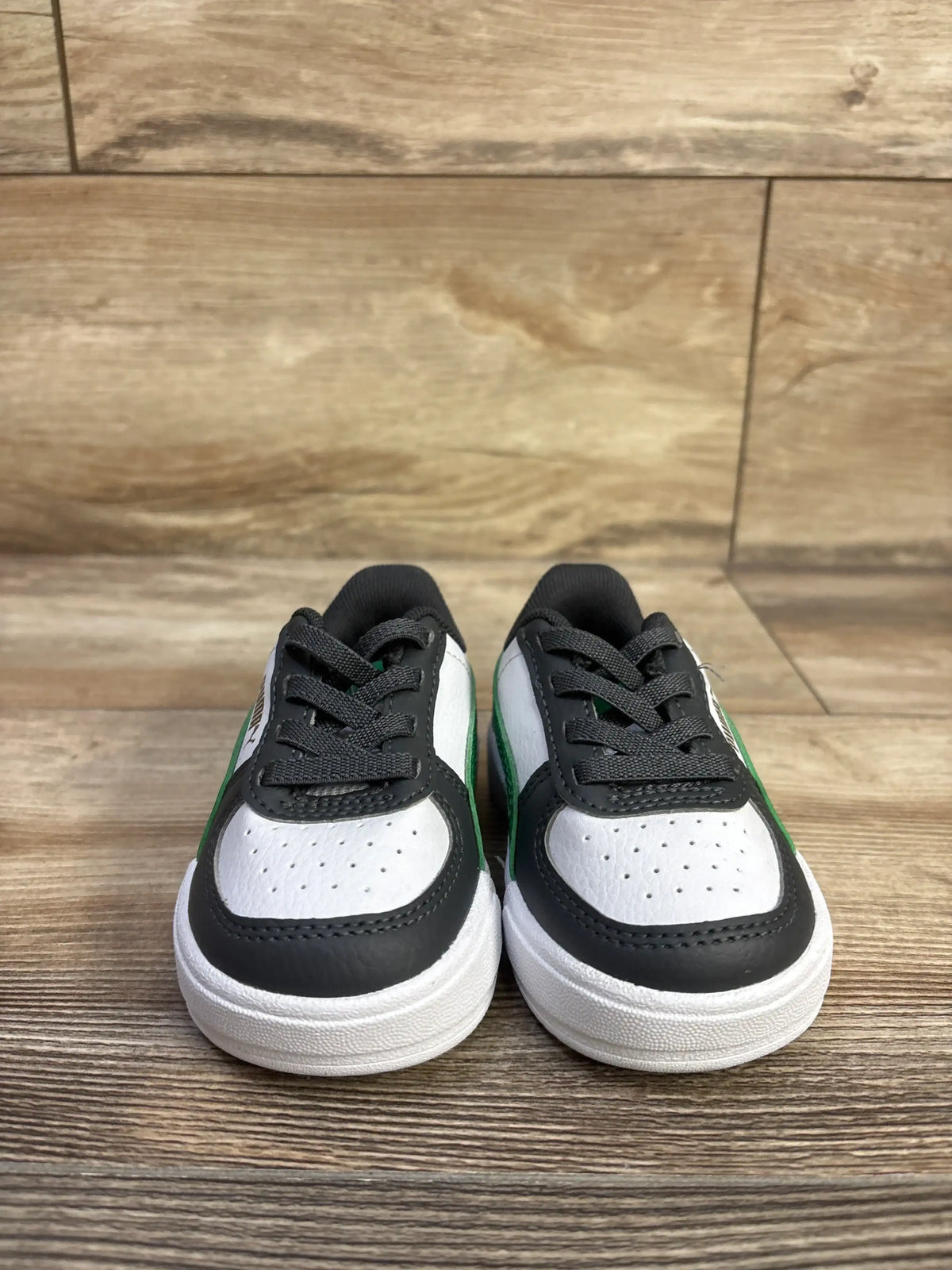 Front view of Puma Caven 2.0 toddler sneaker showcasing white toe, black overlays and green side stripe on wood floor