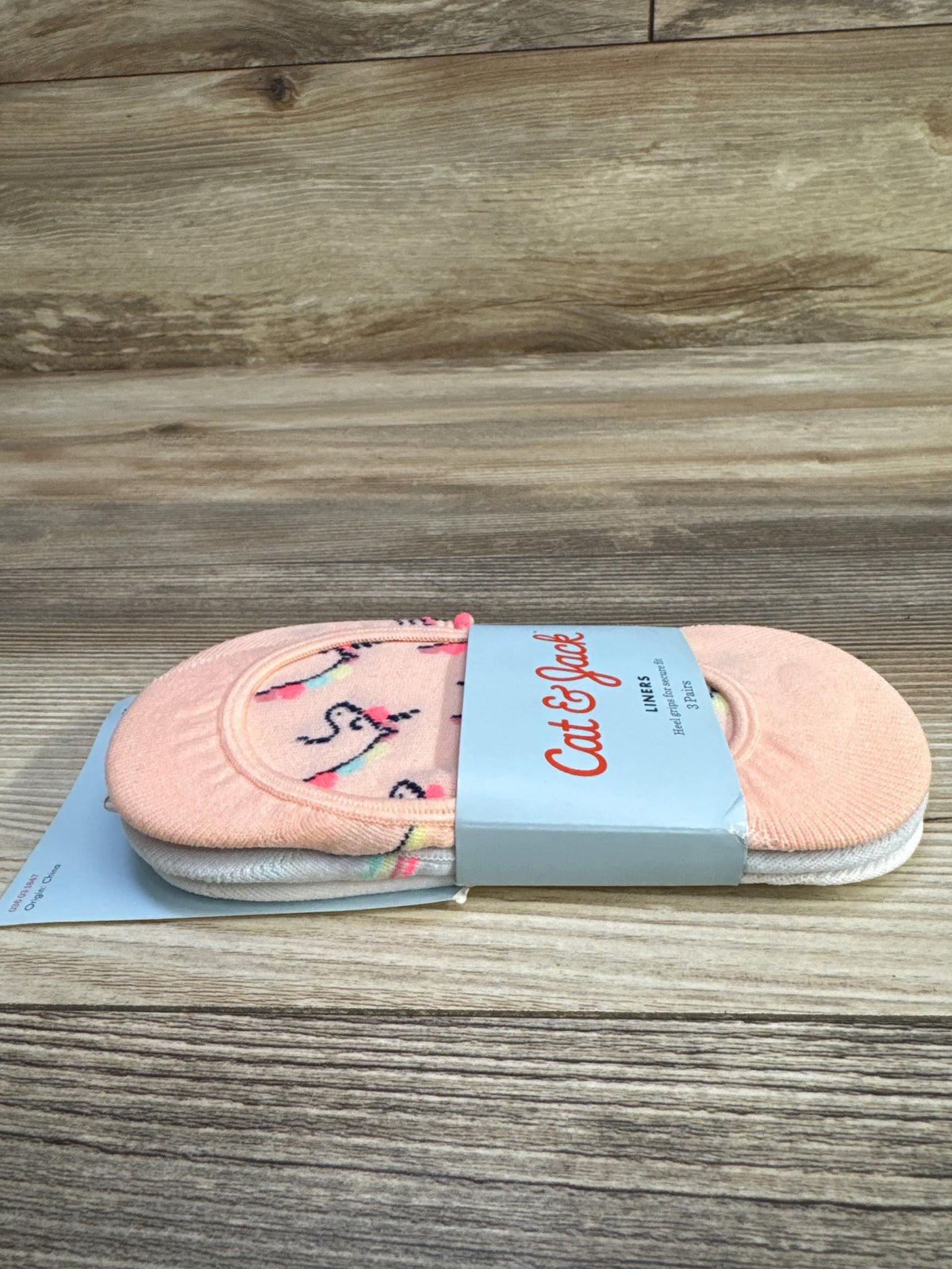 Side view of Cat & Jack sock liner 3-pack showing pink unicorn-patterned liner and branded band on wood background