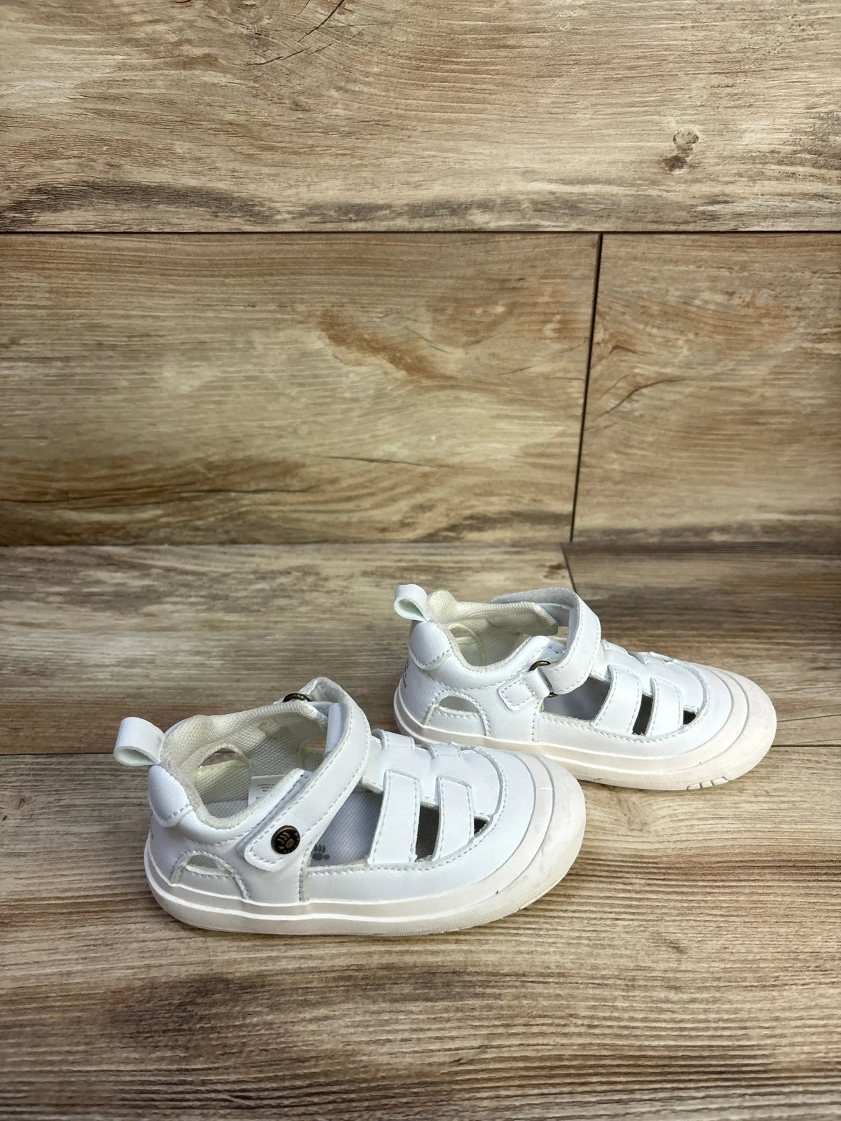 Angled top view of Bearpaw toddler fisherman sandals in white showing closed-toe straps and Velcro ankle strap on wood floor