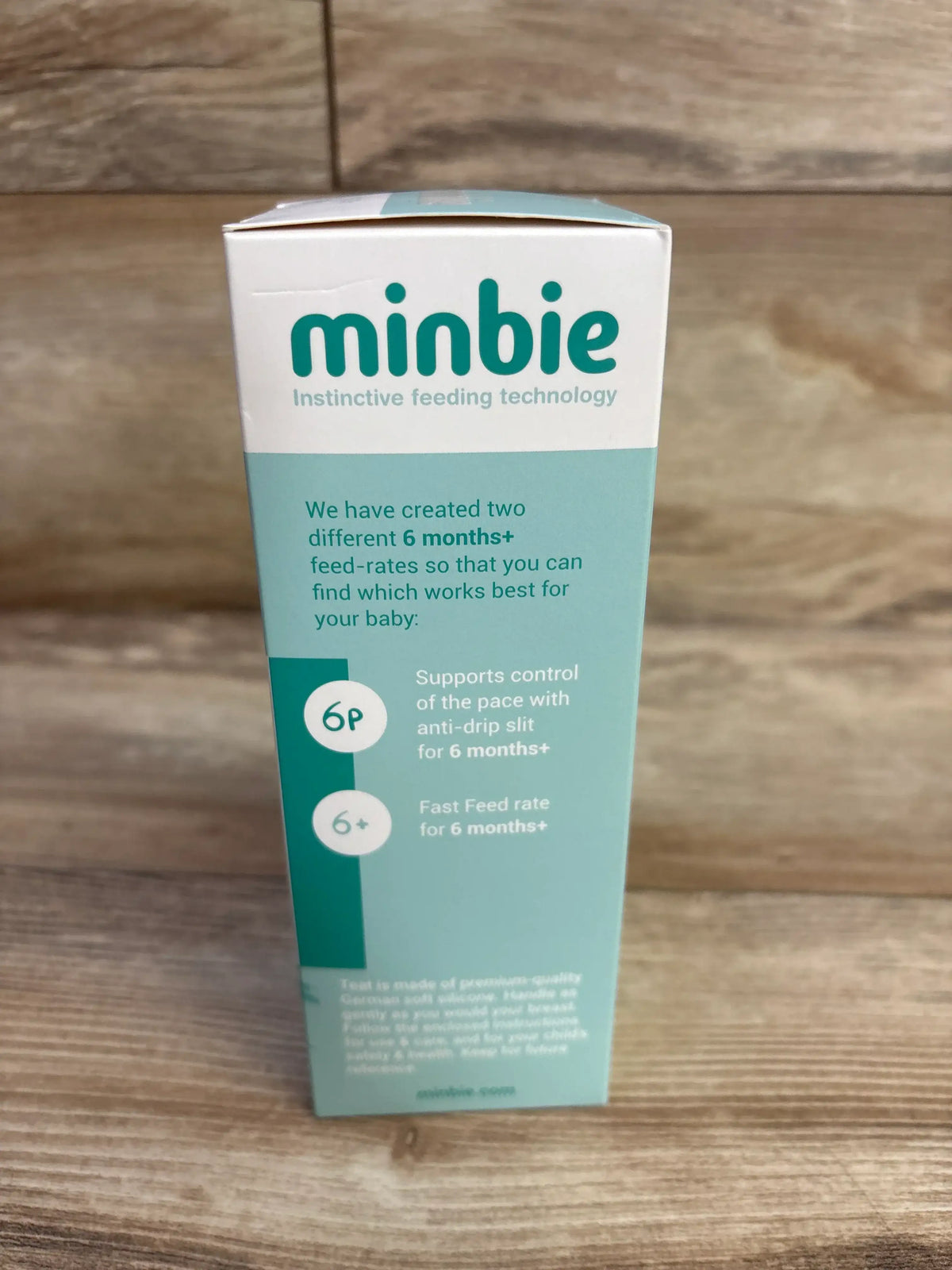 Front view of Minbie 6m+ feeding kit box showing printed 6 months+ feed-rate options and anti-drip slit description on a wooden surface