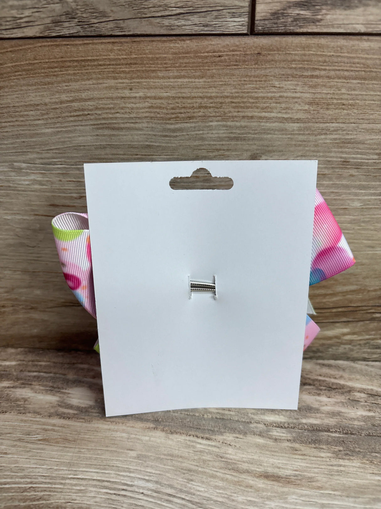 Rear view of large pink balloon hair bow showing pastel tie dye spots and metal clip on white card against wood background