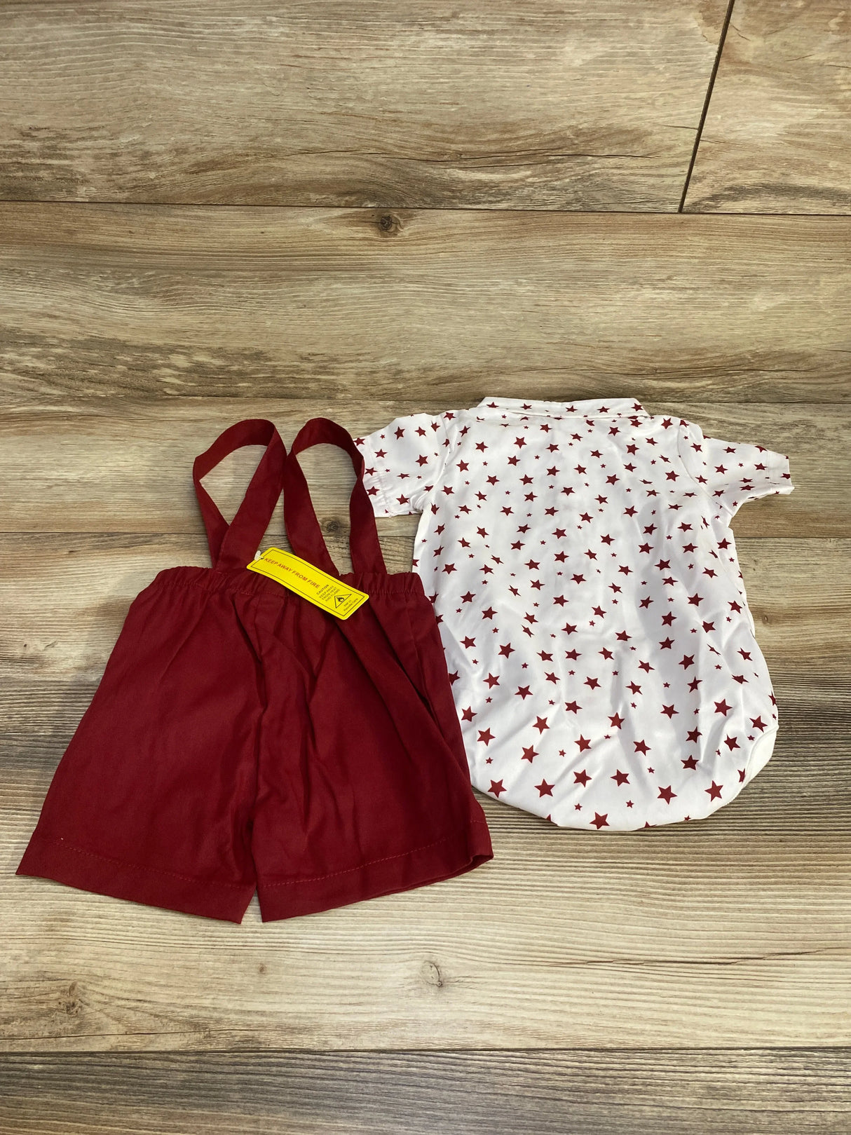 Flat lay of baby white short-sleeve star-print bodysuit and red suspender shorts on wood background