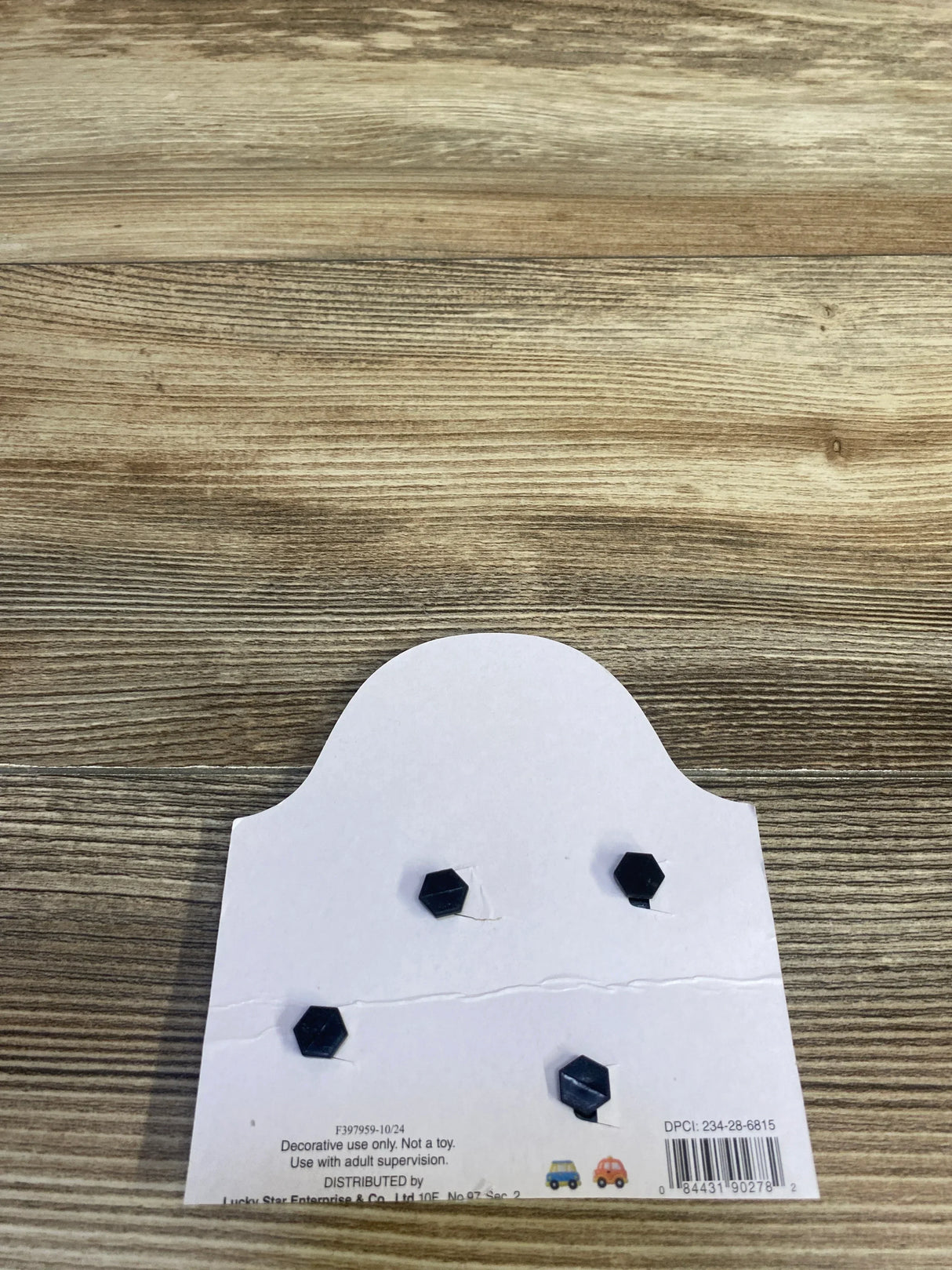 Overhead view of 4-pack black hexagon charms on white display card, glossy finish, on wood tabletop