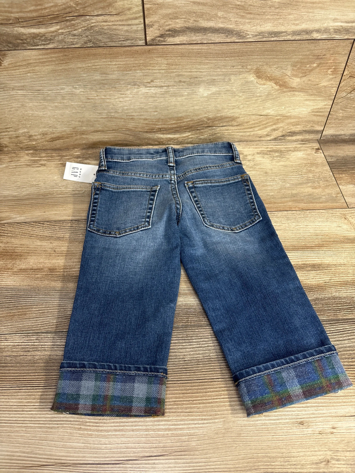Kids denim jeans with plaid cuffed hems and back pockets on wood floor