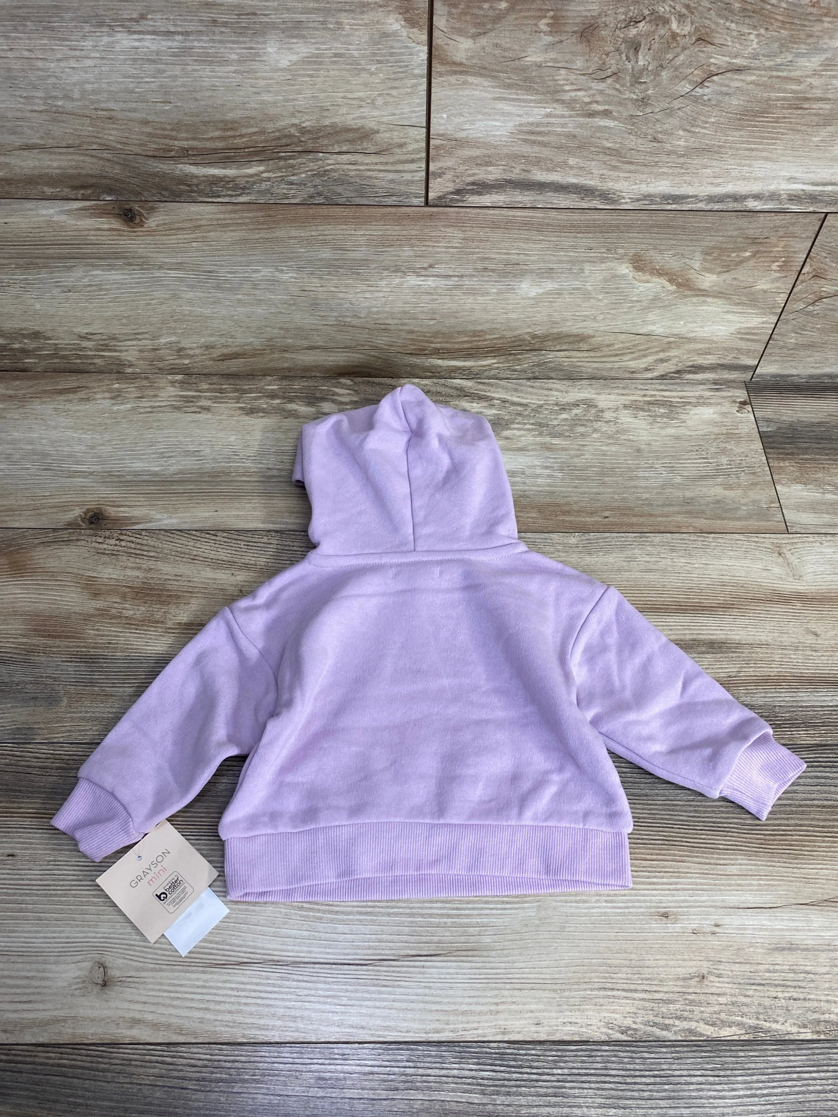 Light purple baby hoodie with tag, long sleeves, laid flat on wood background