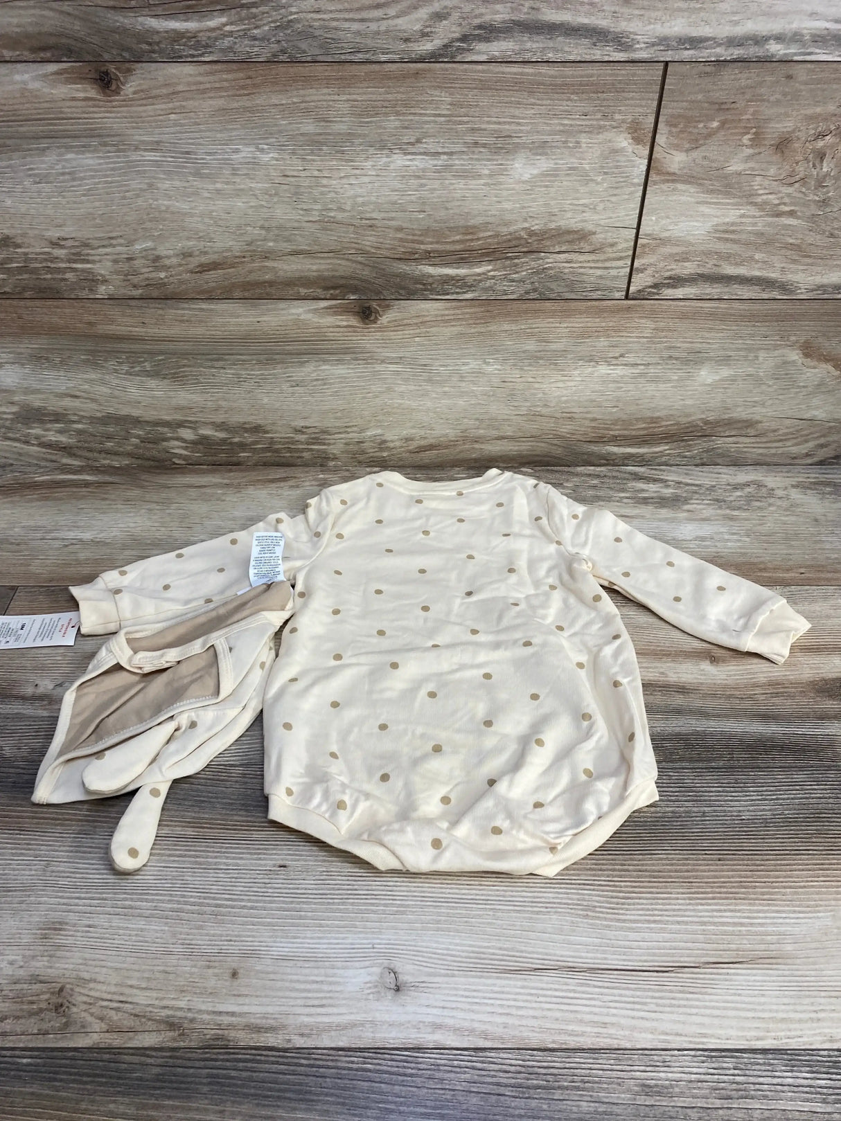 Flat lay of cream polka dot baby romper with matching bonnet showing long sleeves and snap bottom on wood background
