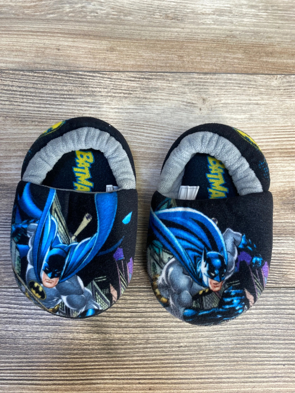 Kids' black Batman slippers with cartoon graphics on wood background