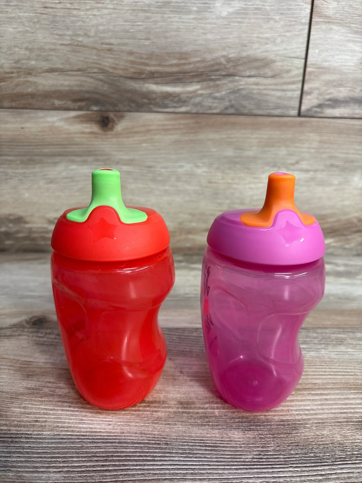 Red and pink toddler sippy cups with lids on wood background