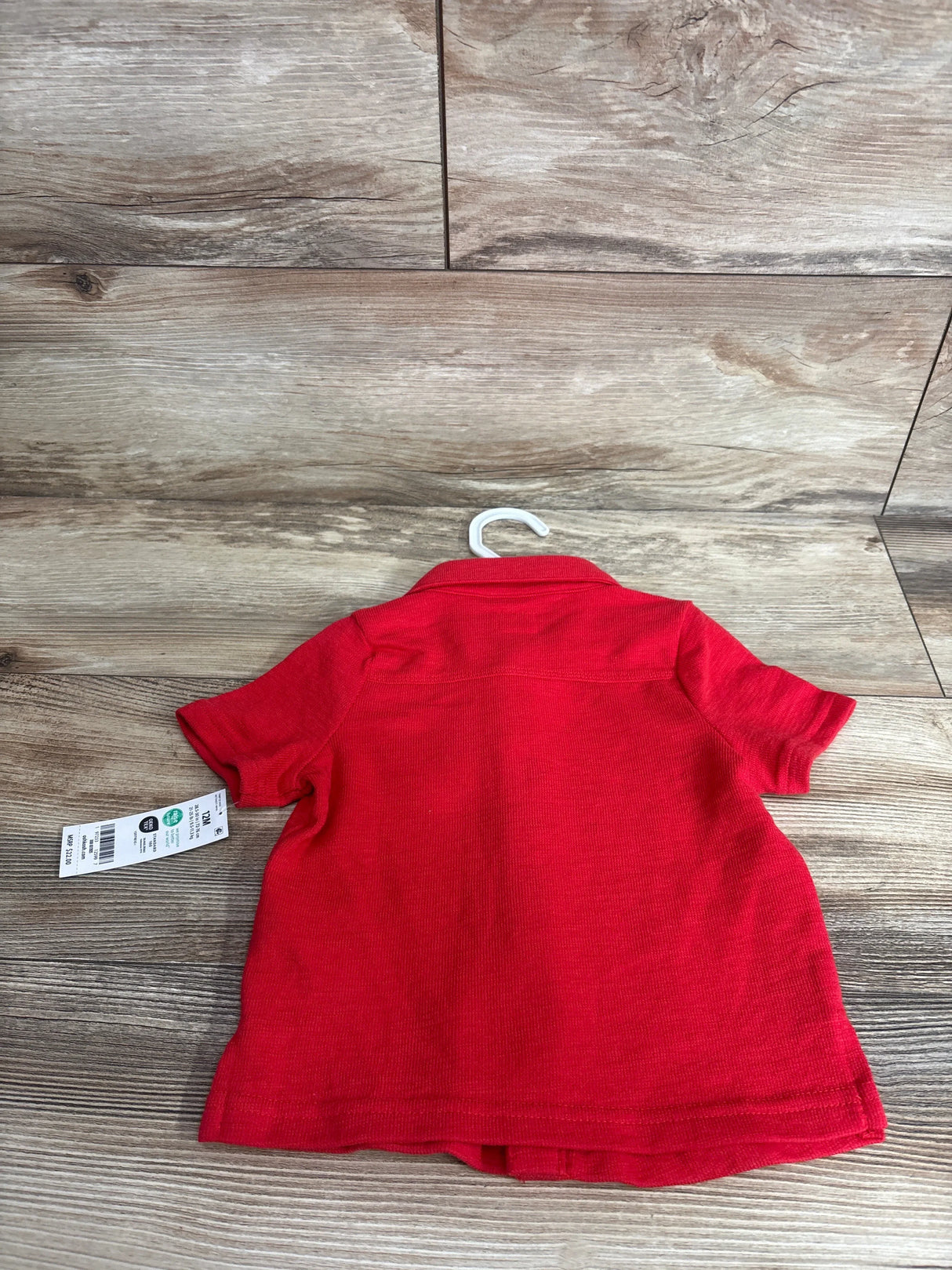 Back view of NEW OshKosh button-up shirt in red, size 12M, showing collar and short sleeves on a wood-look background