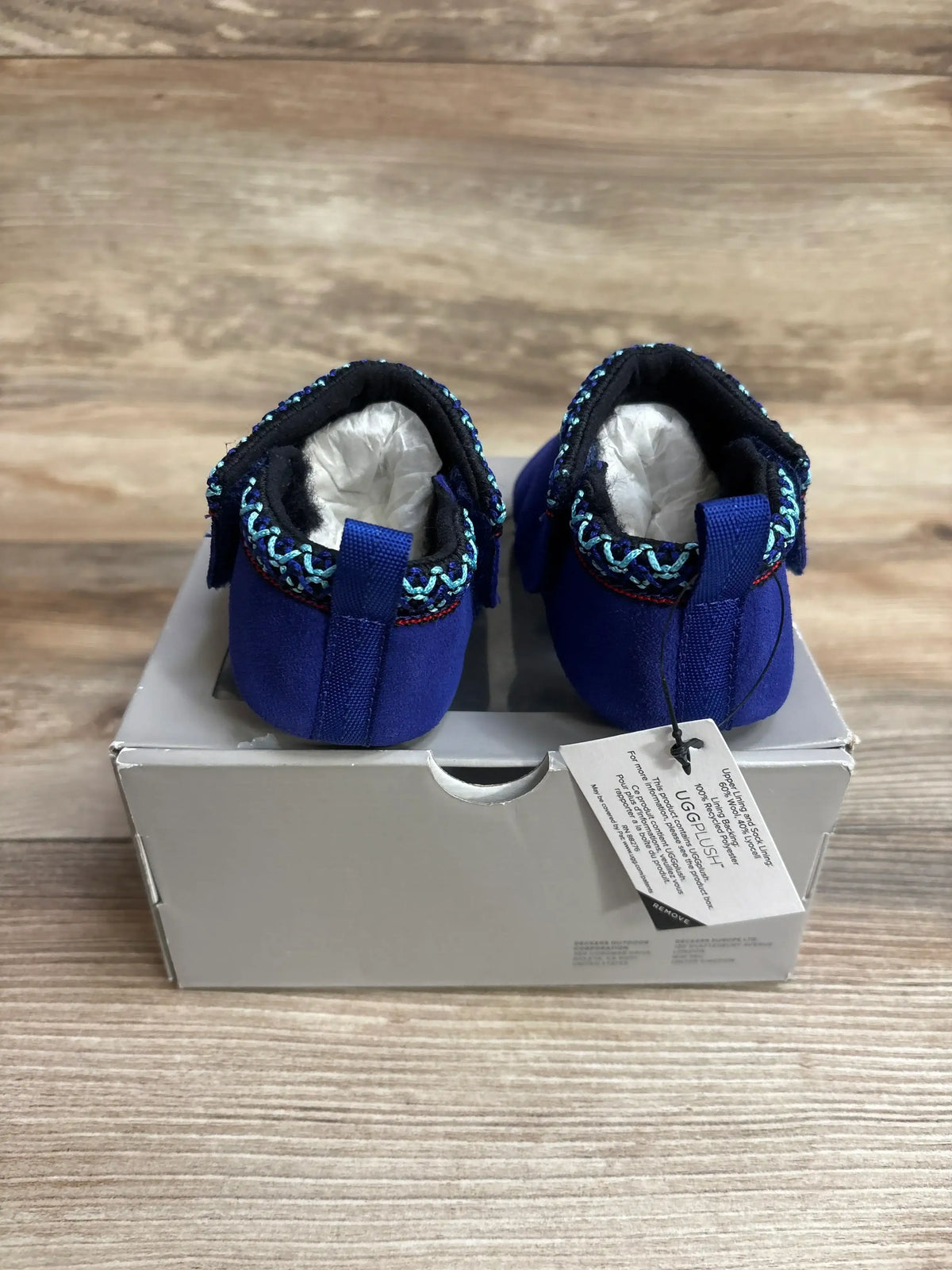 Pair of blue baby moccasins with decorative trim, displayed on a box on wood background