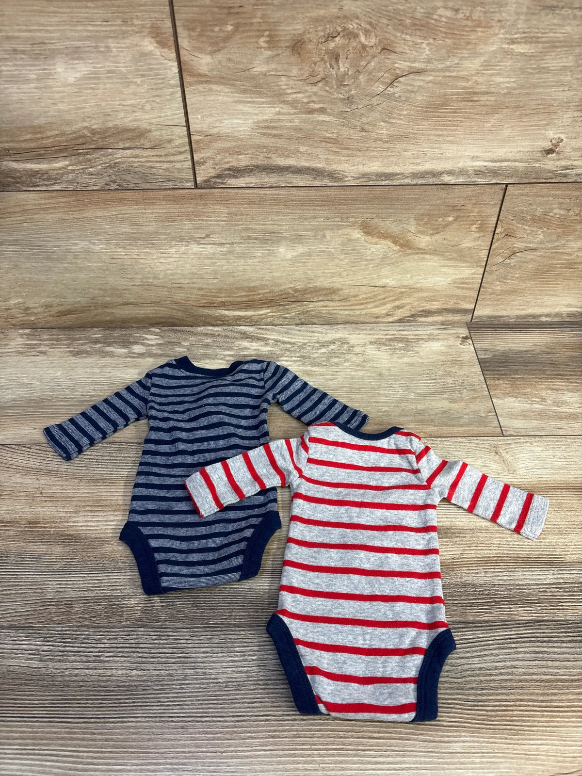 Top-down view of Child Of Mine 2pk Bodysuits Grey sz Preemie showcasing striped long sleeves on a wood-look floor