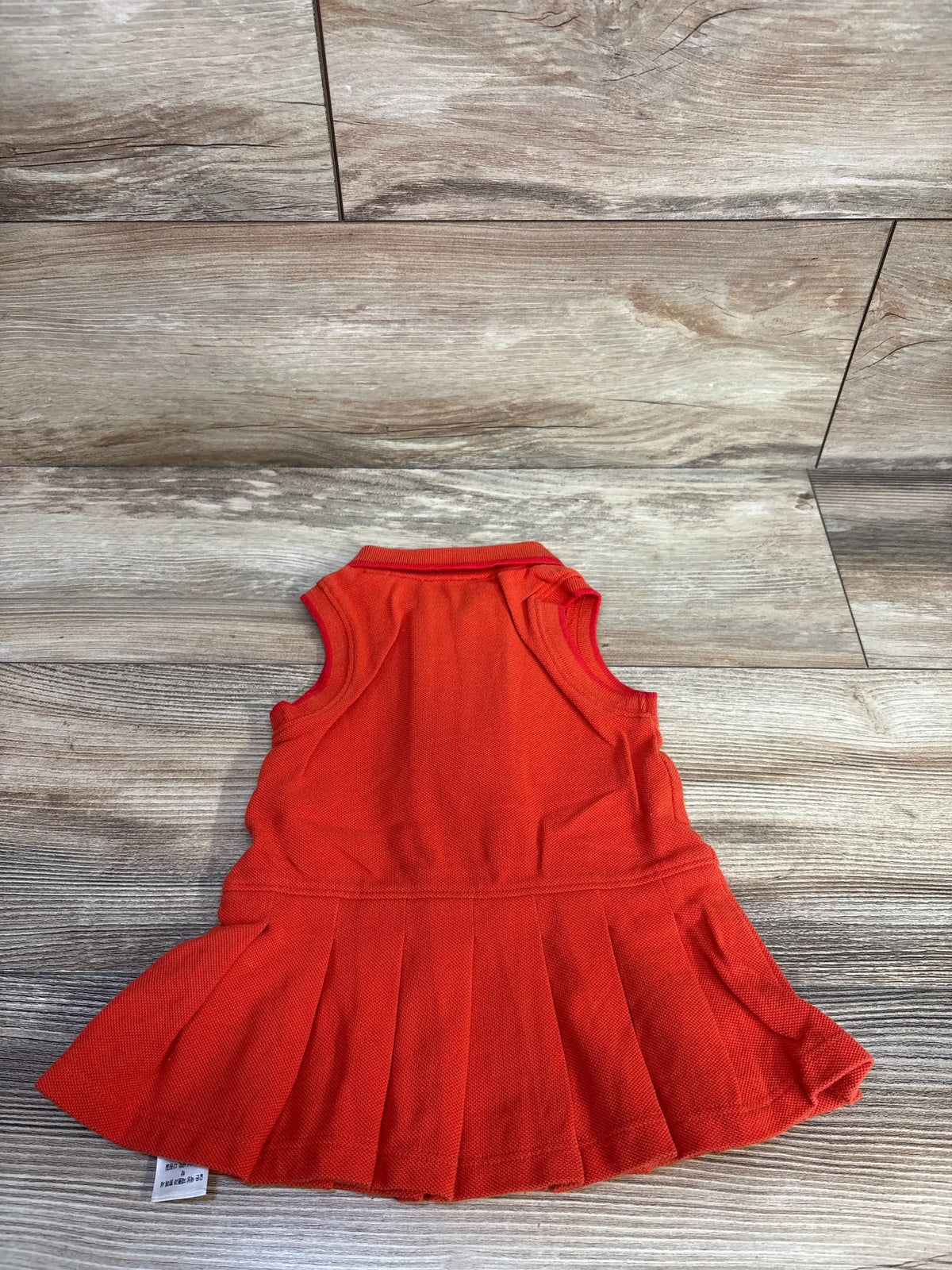 Back view of Burberry Martina polo dress, orange, size 6 months, showing sleeveless knit bodice and pleated skirt on wood floor background