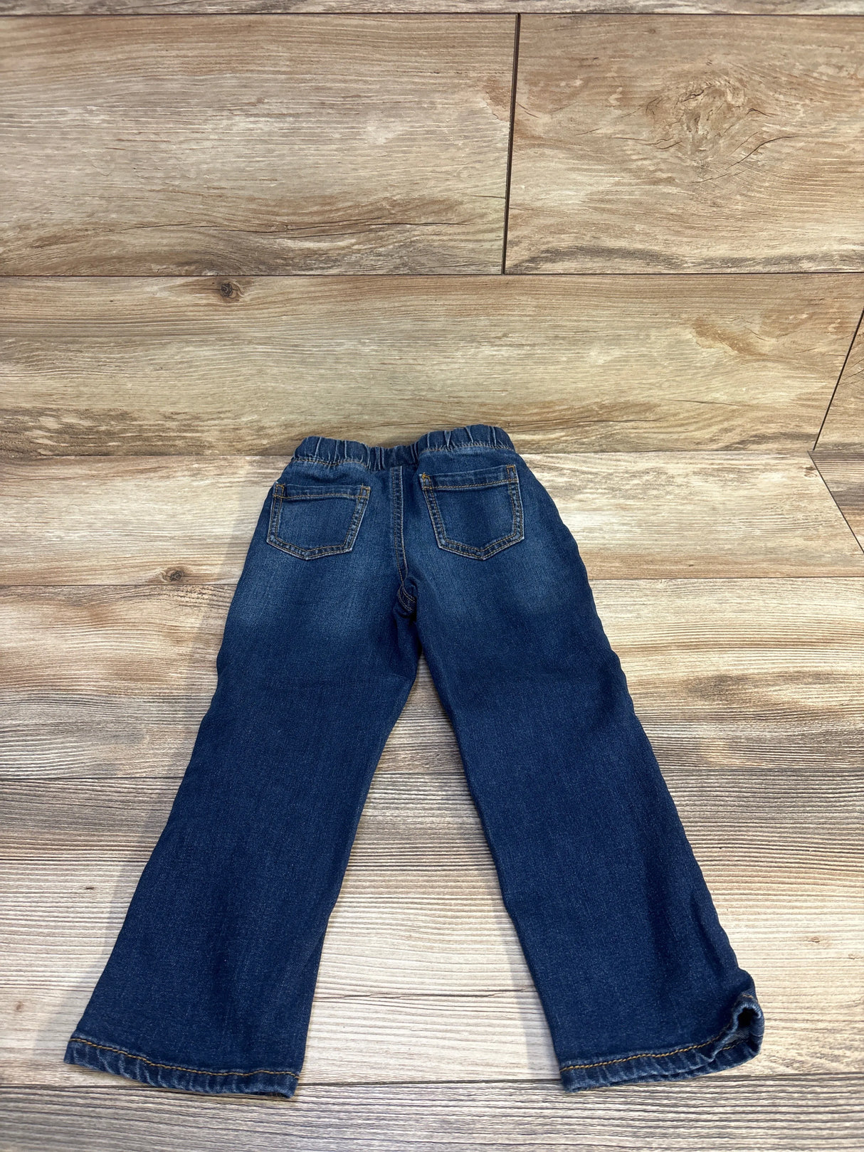Back view flat lay of Jumping Beans toddler blue jeans showing elastic drawstring waist and back pockets on wood background