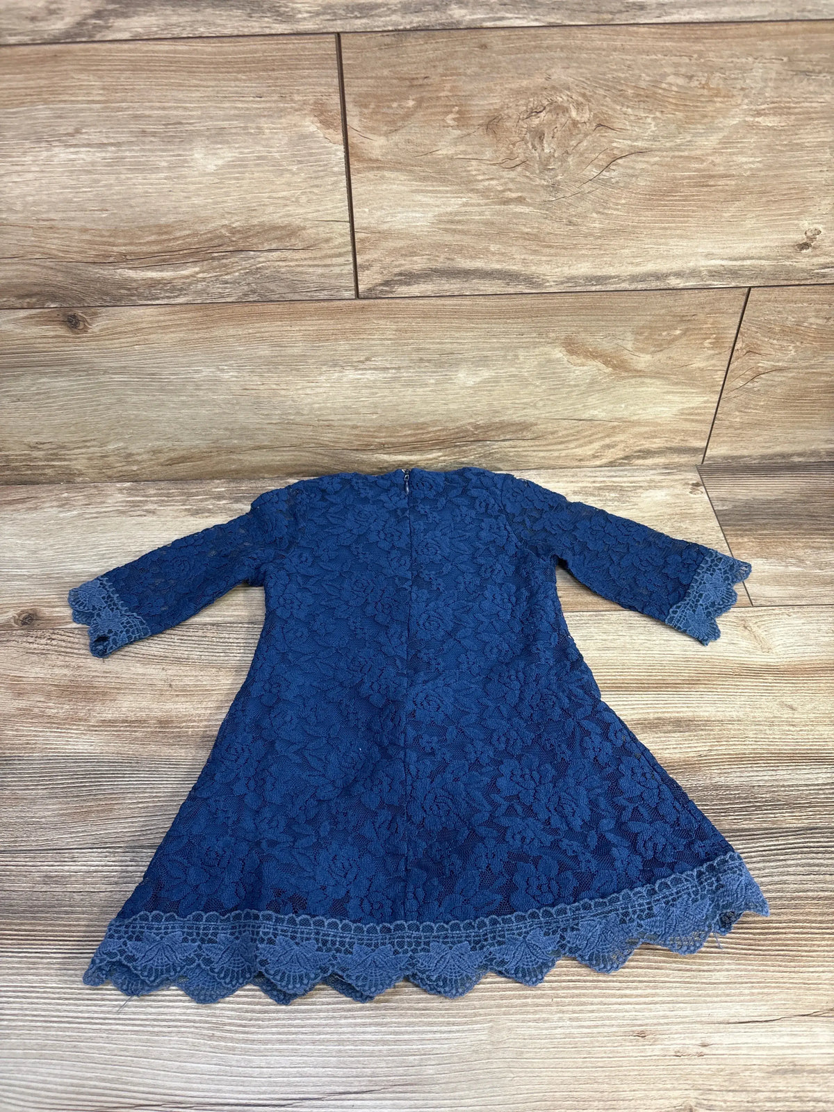Top-down view of blue long sleeve lace dress in size 18-24 months with floral lace and scalloped hem on wood-look flooring