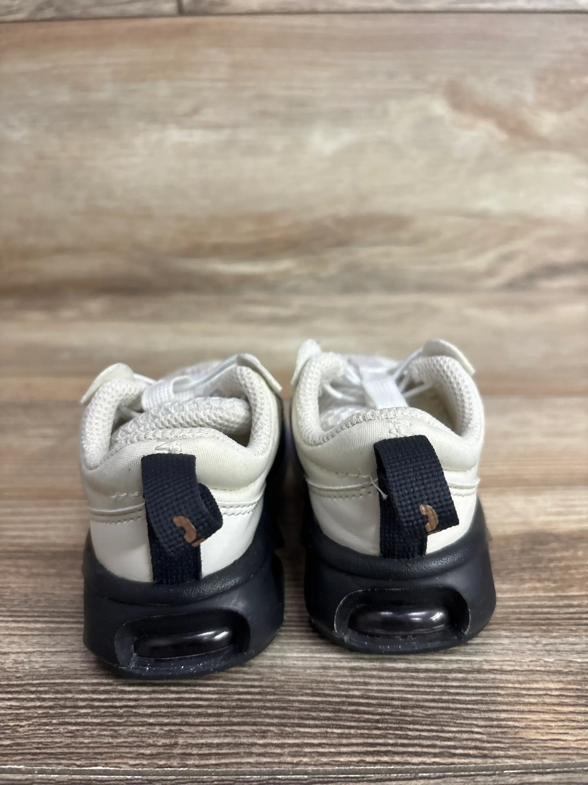 Rear view of Nike Air Max 2021, size 3C, showing cream upper and black midsole with visible Air unit on wood background