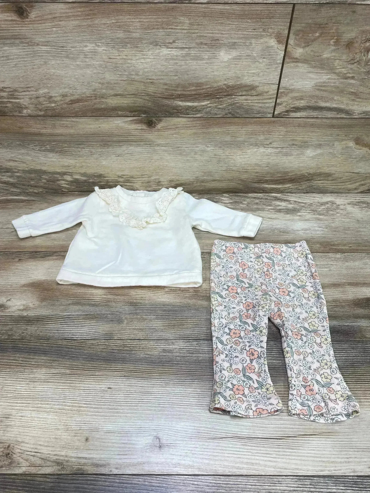 Flat lay of Nicole Miller cream sweatshirt with ruffle collar and floral leggings with ruffle hem on wood background