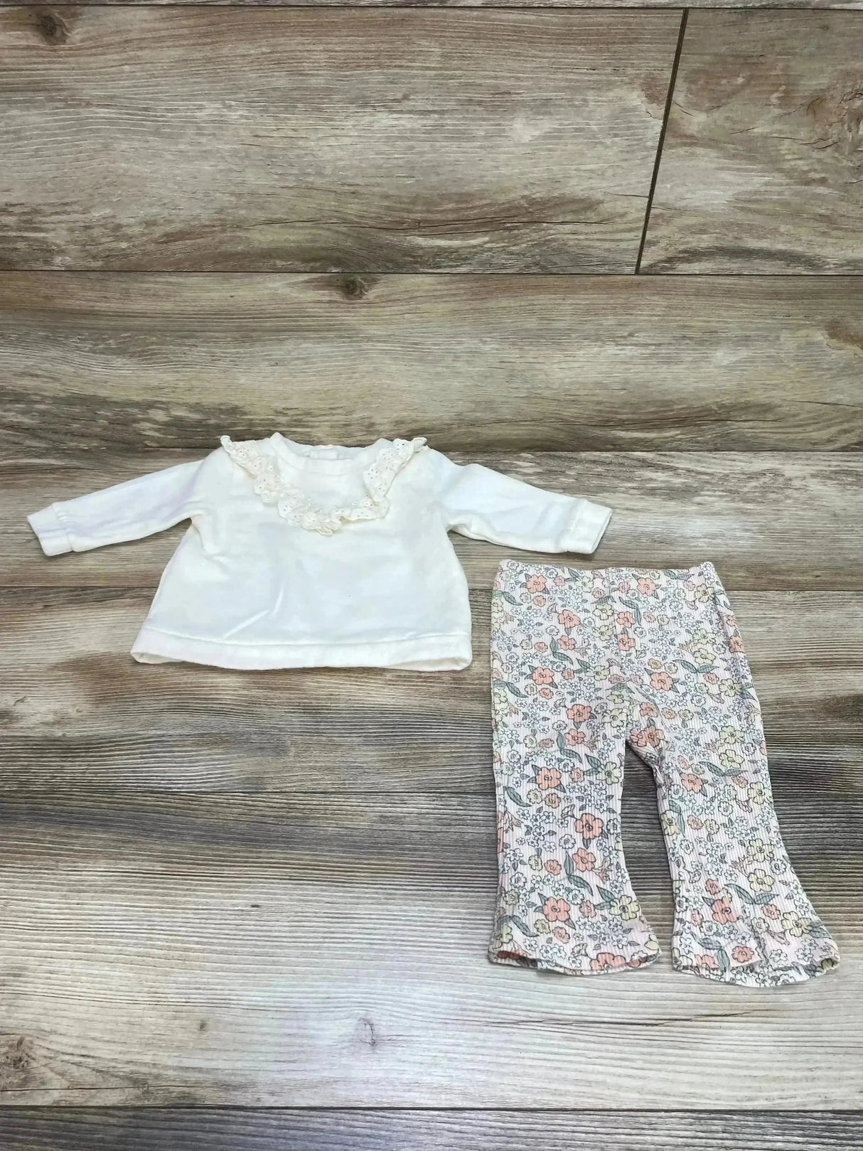 Flat lay of Nicole Miller cream sweatshirt with ruffle collar and floral leggings with ruffle hem on wood background