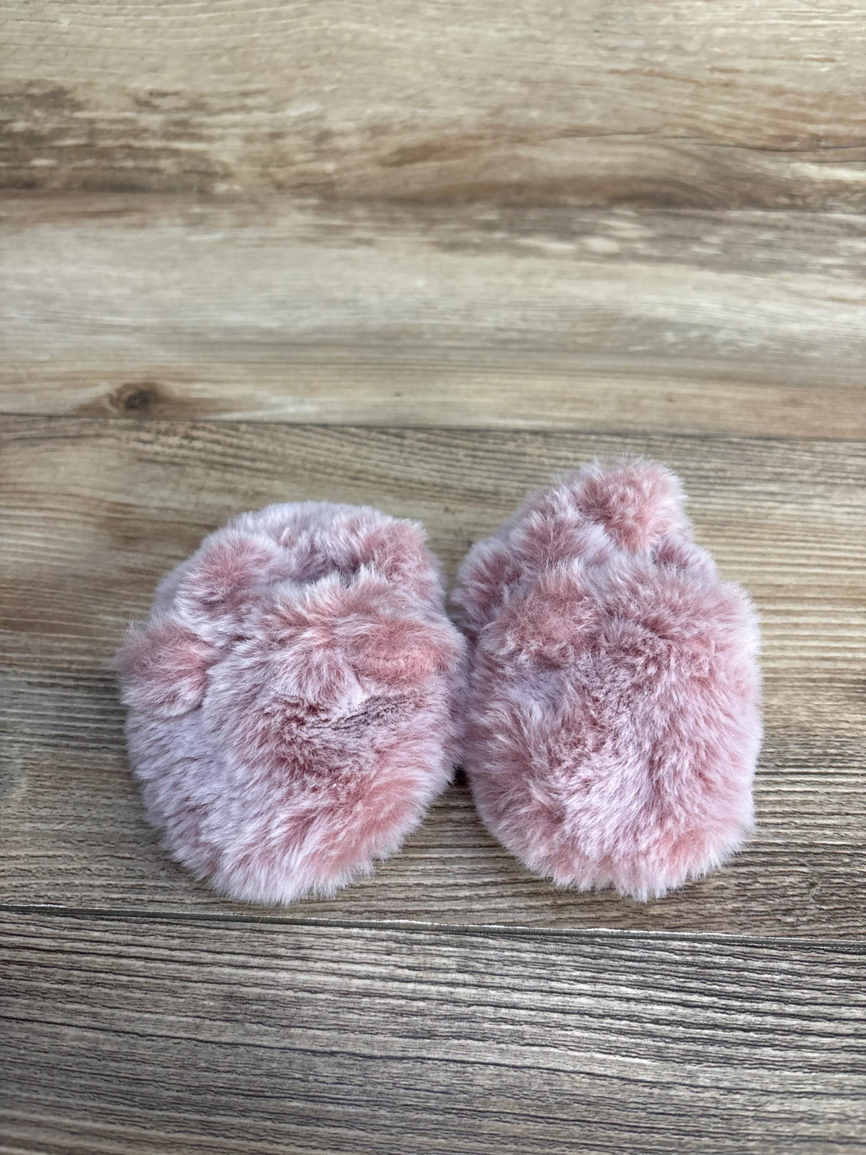 Top view of Just One You faux fur baby booties, size 1/2C, in soft pink showing fluffy plush texture on wood background