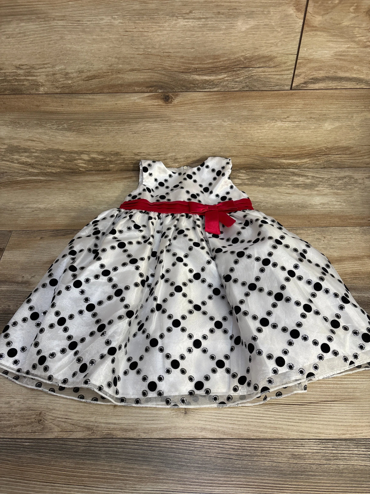 Flat lay of white polka dot toddler dress size 3T showcasing red sash bow and full skirt on wood floor