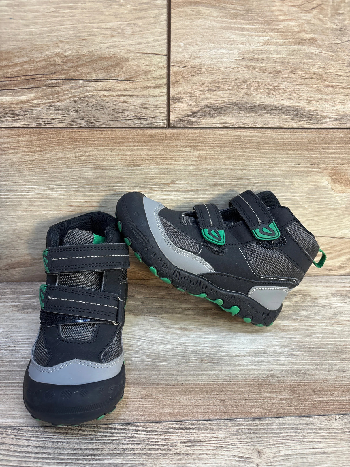 Kids black and gray hiking shoes with green accents on wood floor