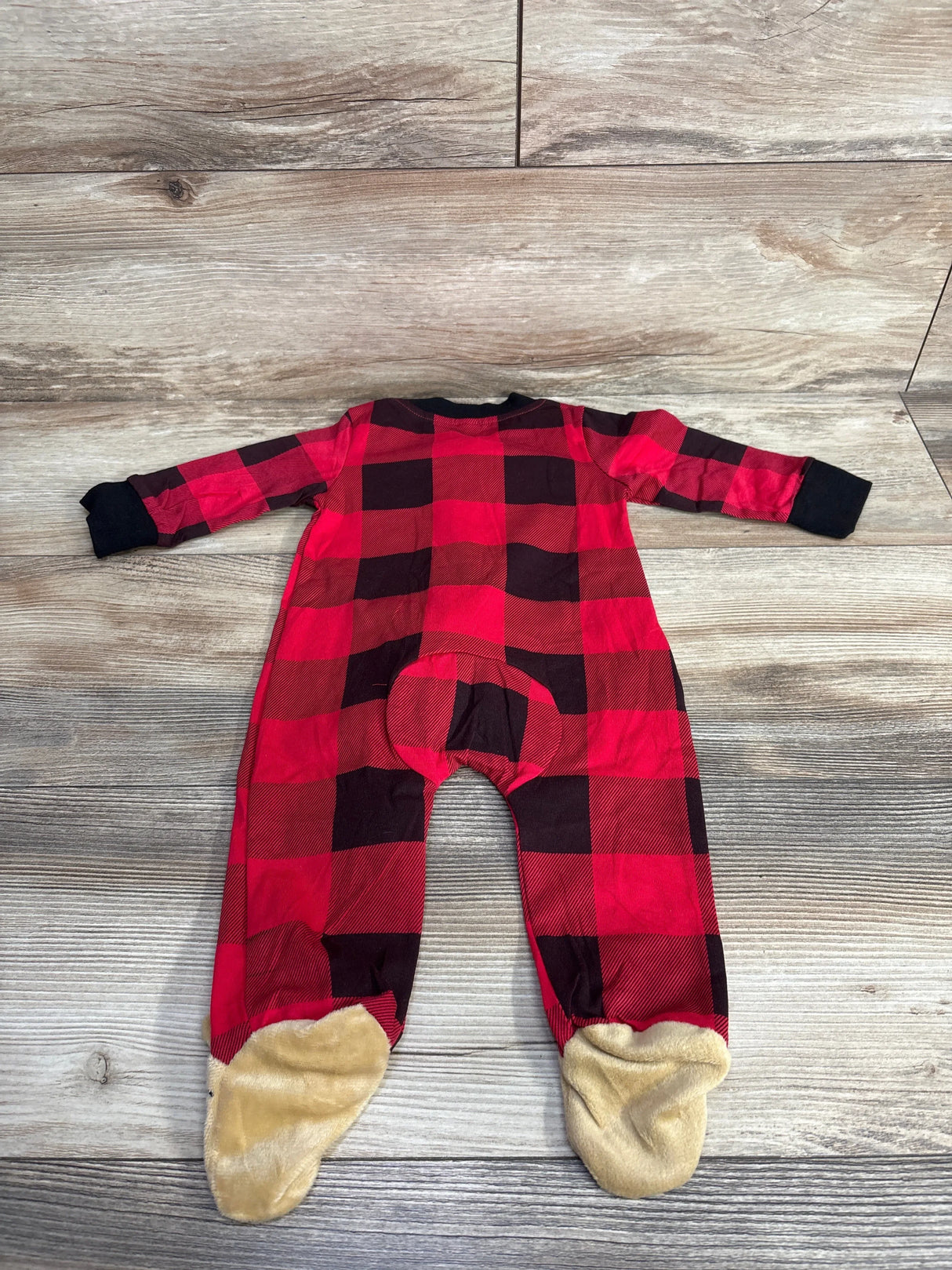 Red and black plaid baby sleeper pajamas with tan footies on wood floor