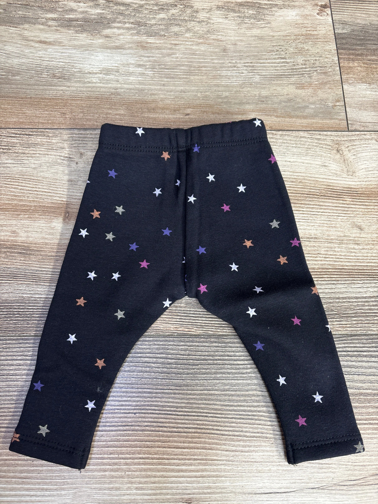 Black baby leggings with colorful star print on wooden floor, children's clothing