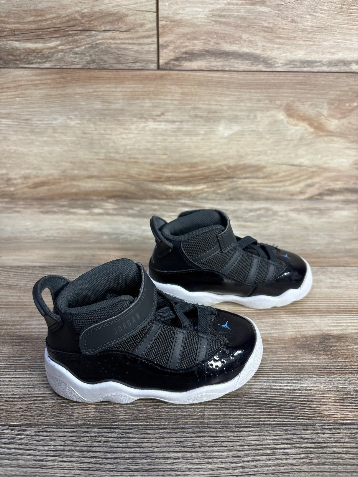 Black toddler Jordan sneakers with white soles on a wooden floor