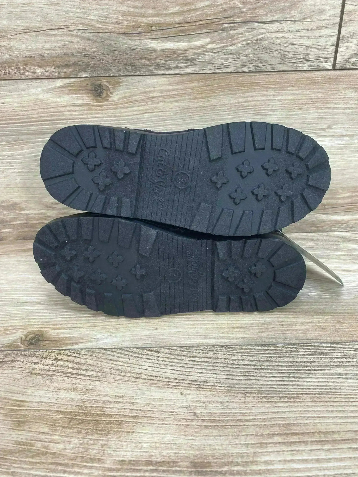 Bottom view of Cat & Jack Ronin kids' black boots showcasing lug soles and tread pattern on wood background