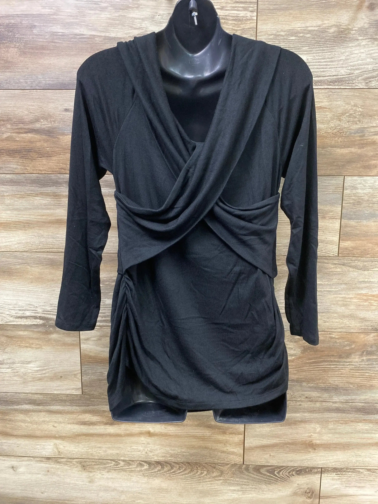 Front view of Isabel maternity black cross-front top with draped neckline, hood, long sleeves and side ruching on wood wall