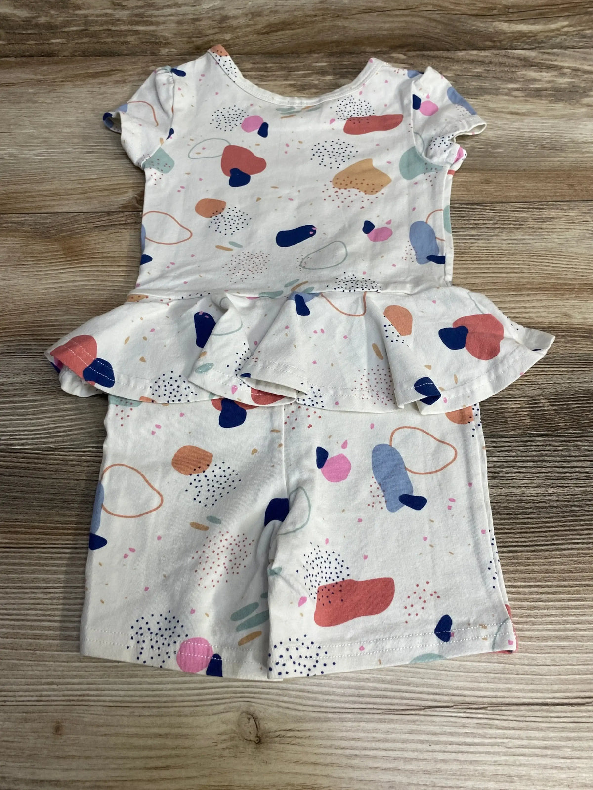 Flat lay of Dot Dot Smile terrazzo print romper size 12-24 months showing peplum skirt and short sleeves on wood background
