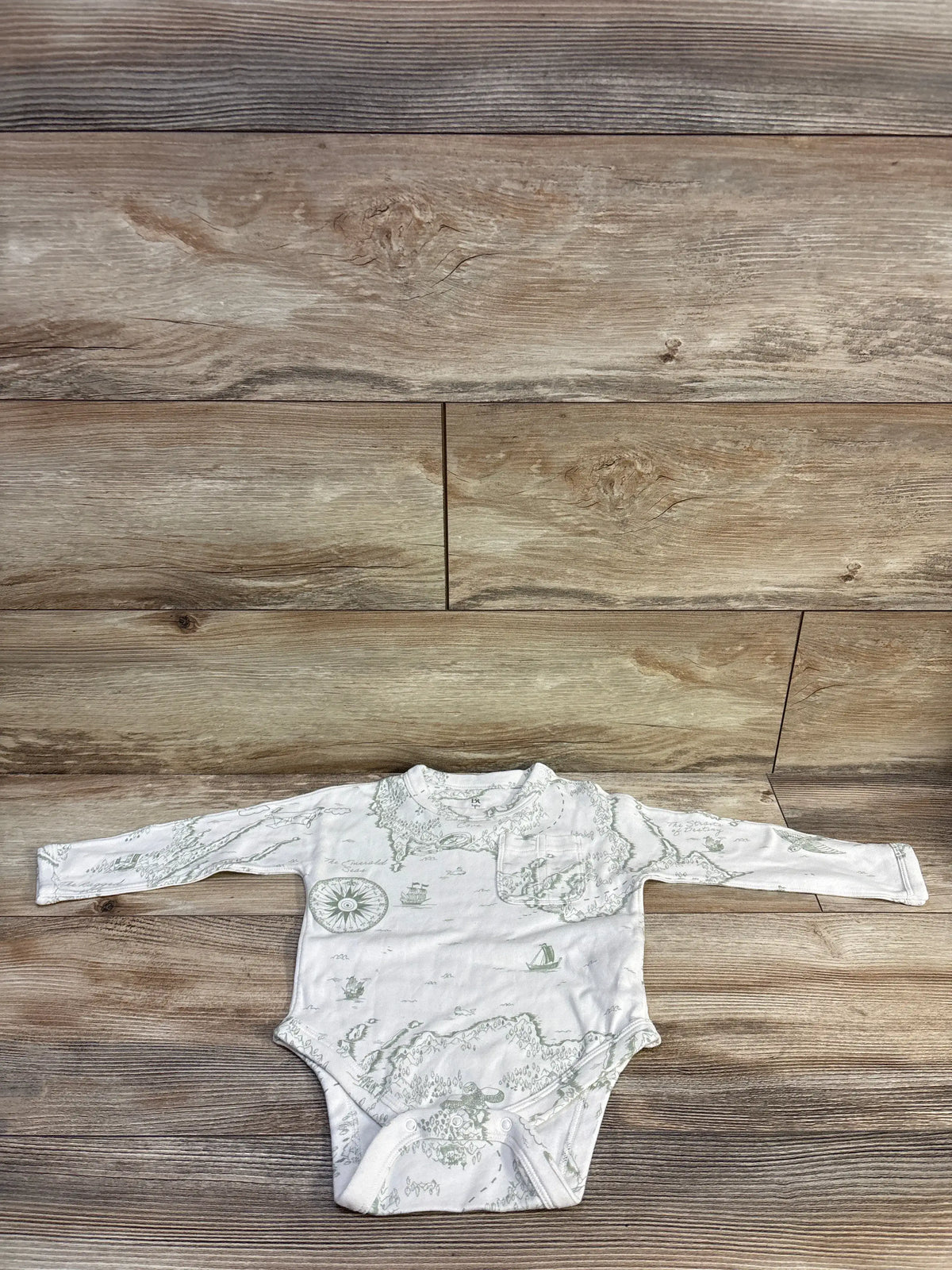 Front view of a white Banana Republic map print bodysuit with long sleeves and snap closures laid flat on a wood pattern floor