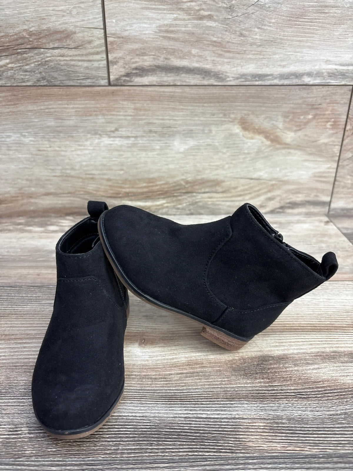 Black suede kids ankle boots with rubber soles on wood background