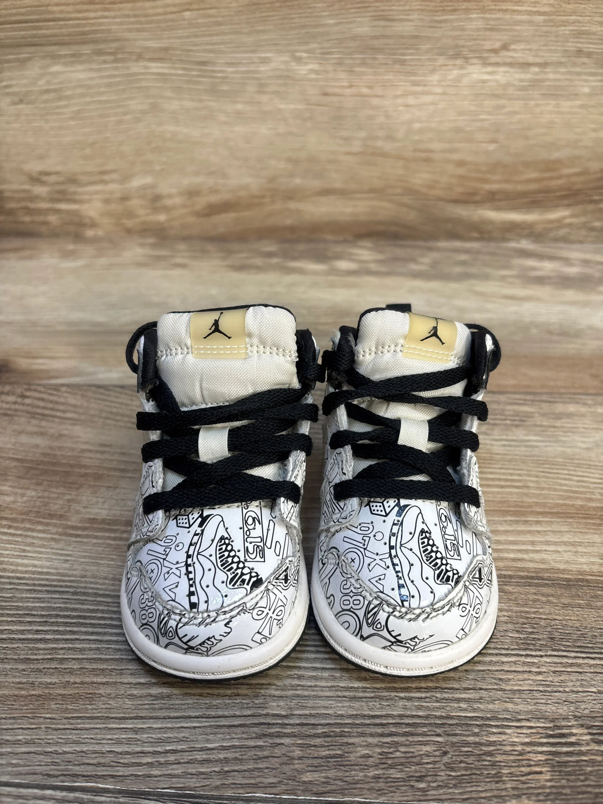 Toddler sneakers with black laces, graphic design, and Jordan logo on wood floor