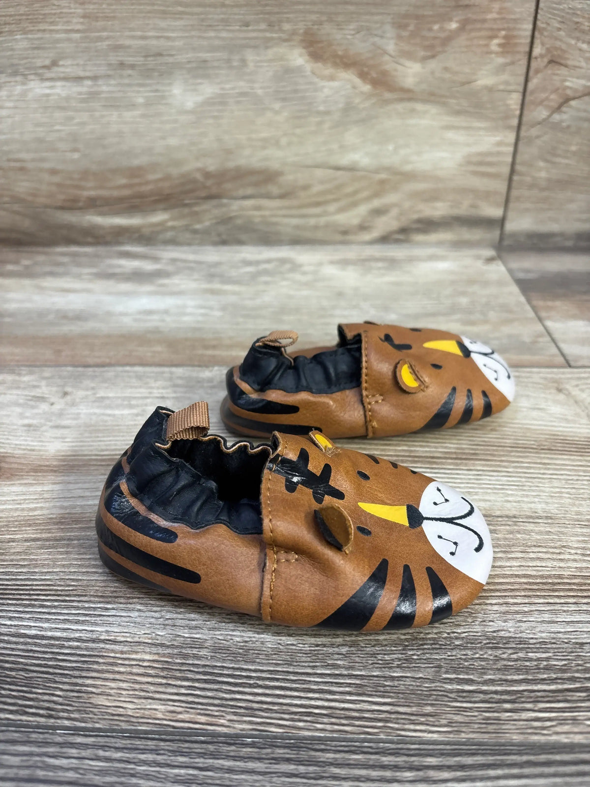 Front three-quarter view of toddler faux-leather tiger soft-sole shoes showing tiger face, elasticized ankle and brown finish on wood