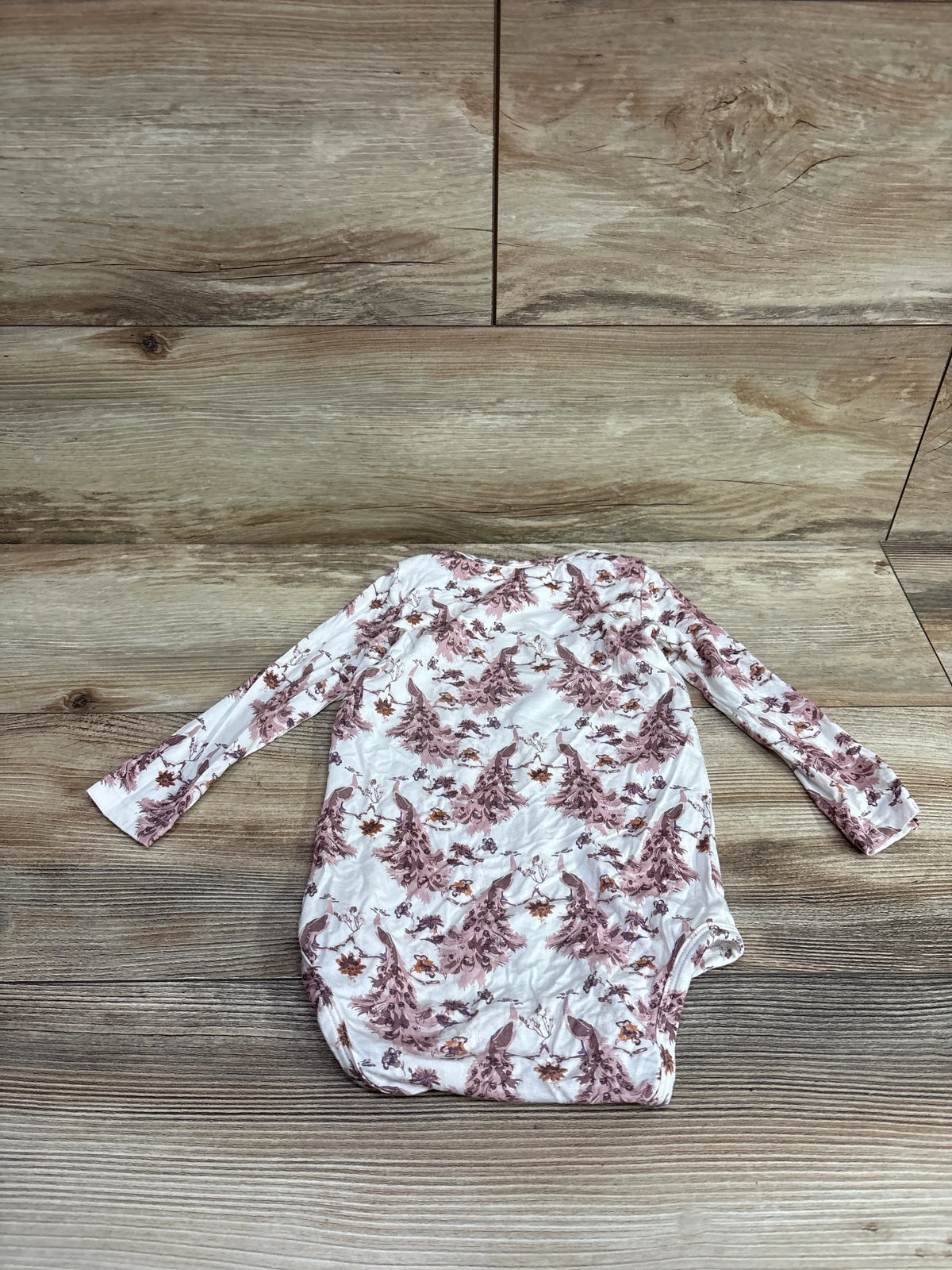 White Kate Quinn long sleeve bamboo bodysuit with mauve floral print on a wood background