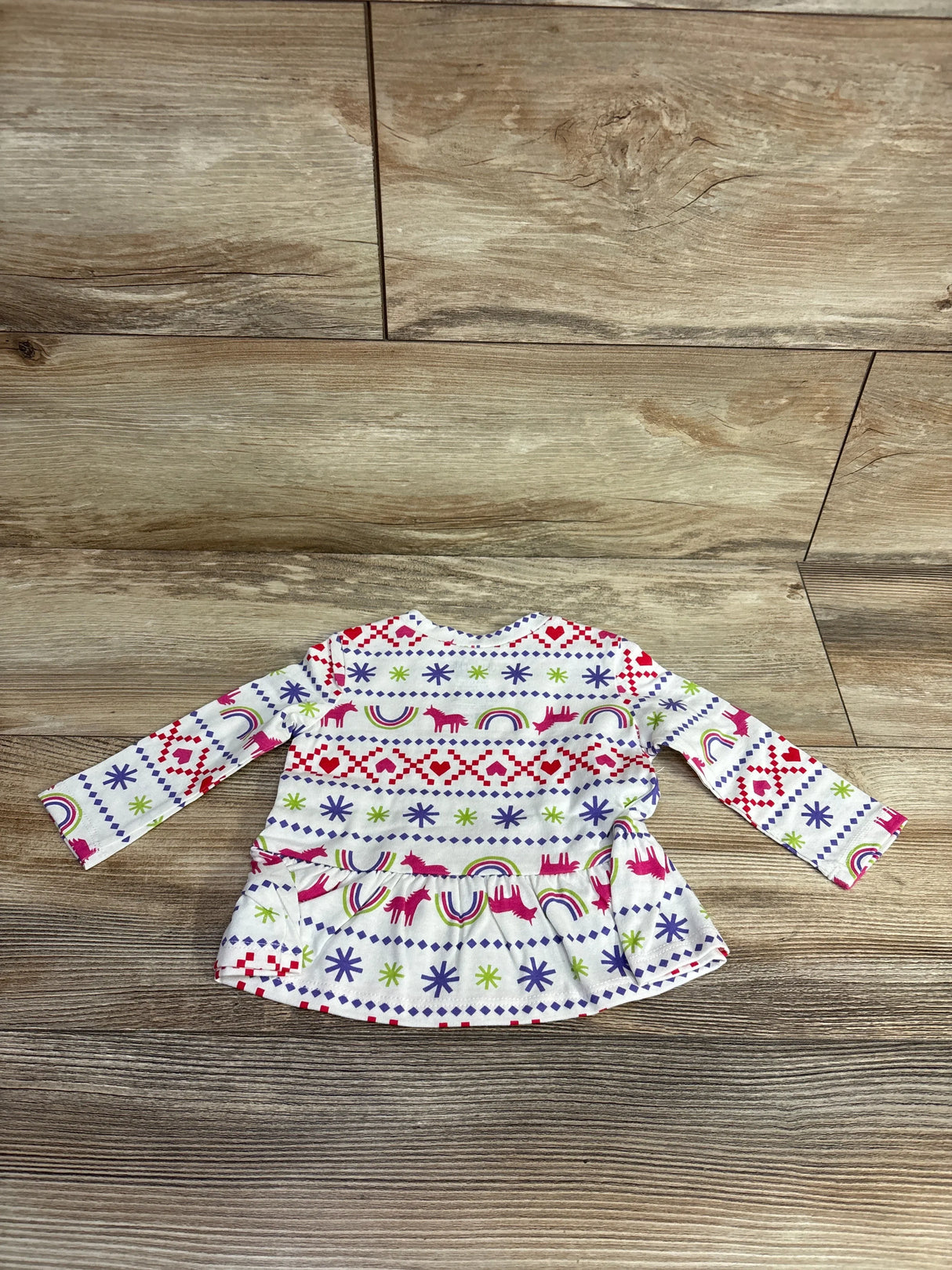 Colorful long-sleeve toddler shirt with heart, unicorn, rainbow, and star patterns on wooden floor