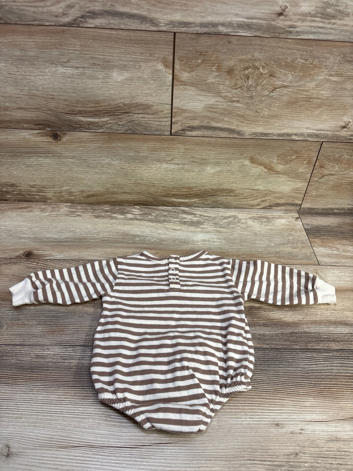 Top-down view of tan and white striped bubble romper with long sleeves and snap placket on a wood floor