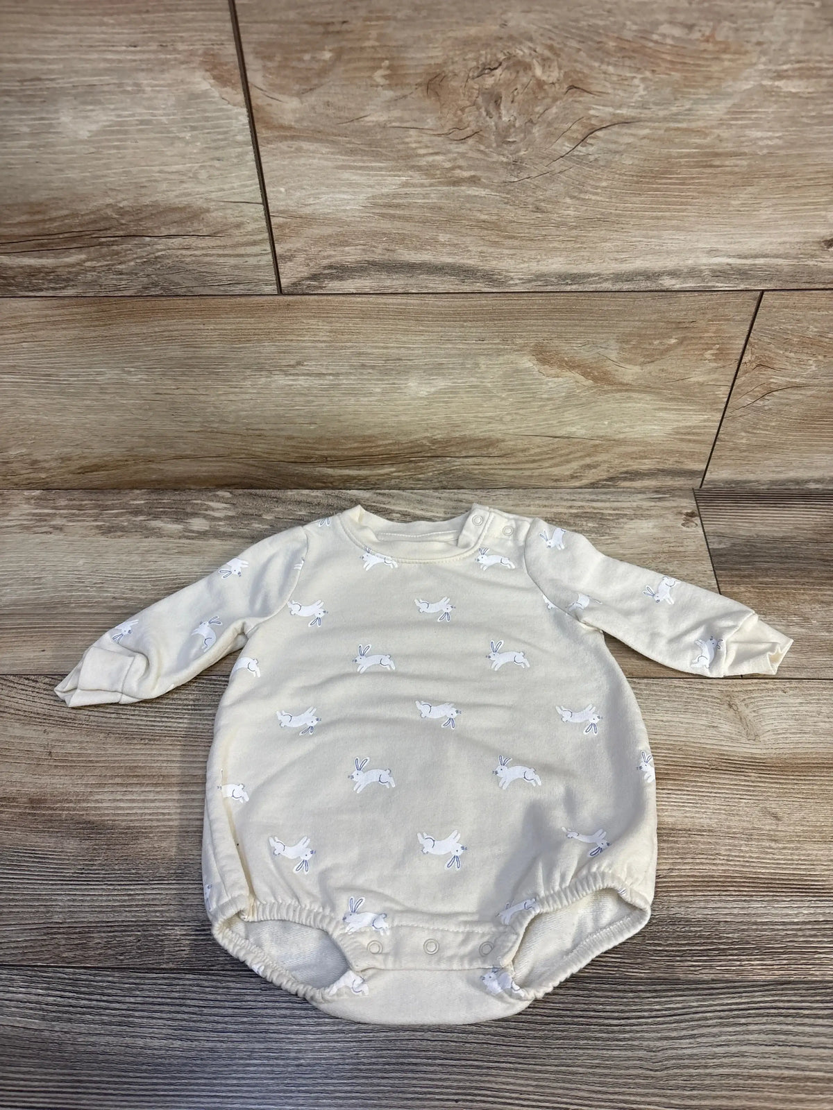 Cream baby bodysuit with bunny print and long sleeves on wood floor