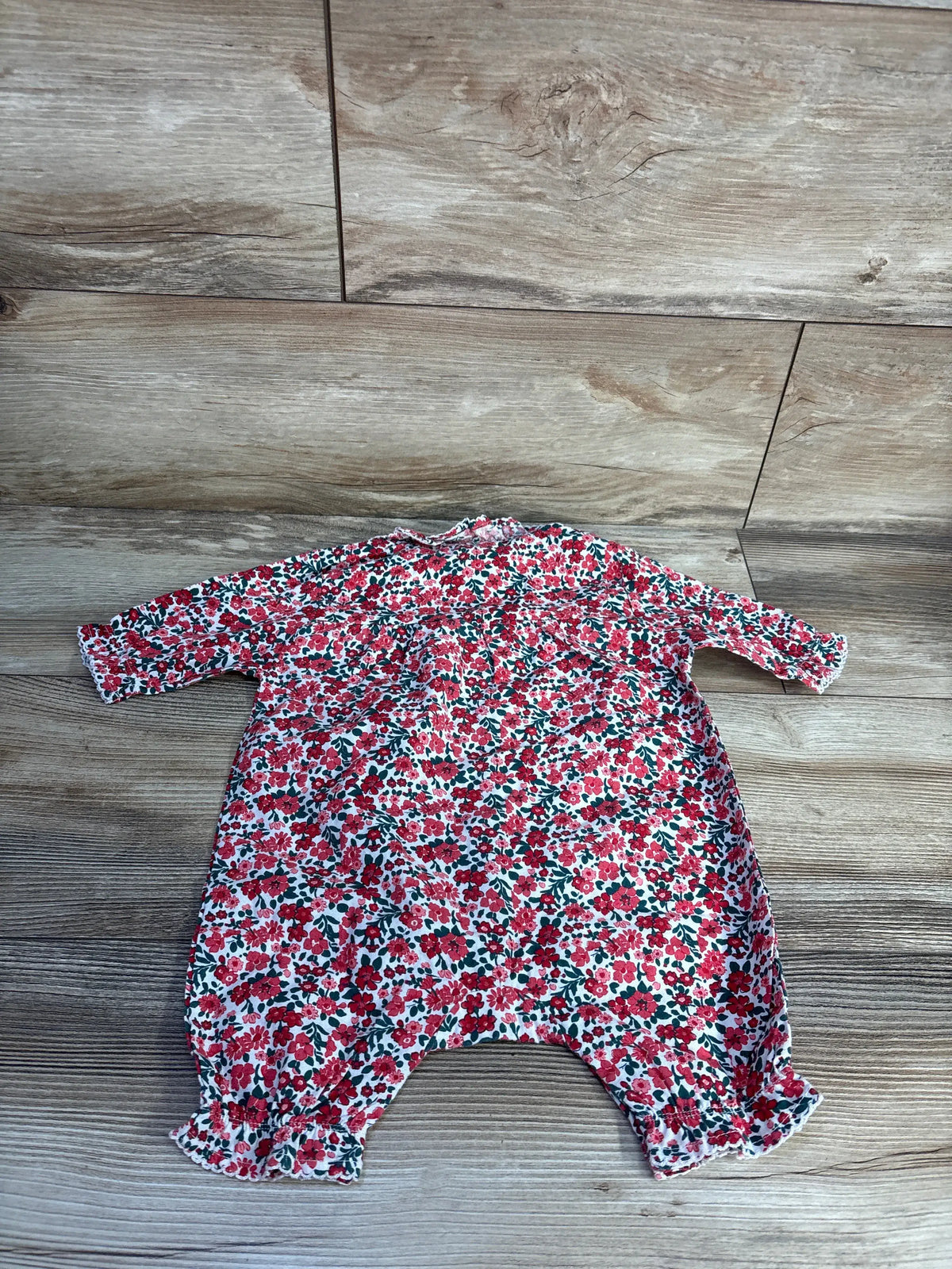 Top-down view of Petite Plume twill floral romper in red, showcasing floral print and long sleeves on a wood floor
