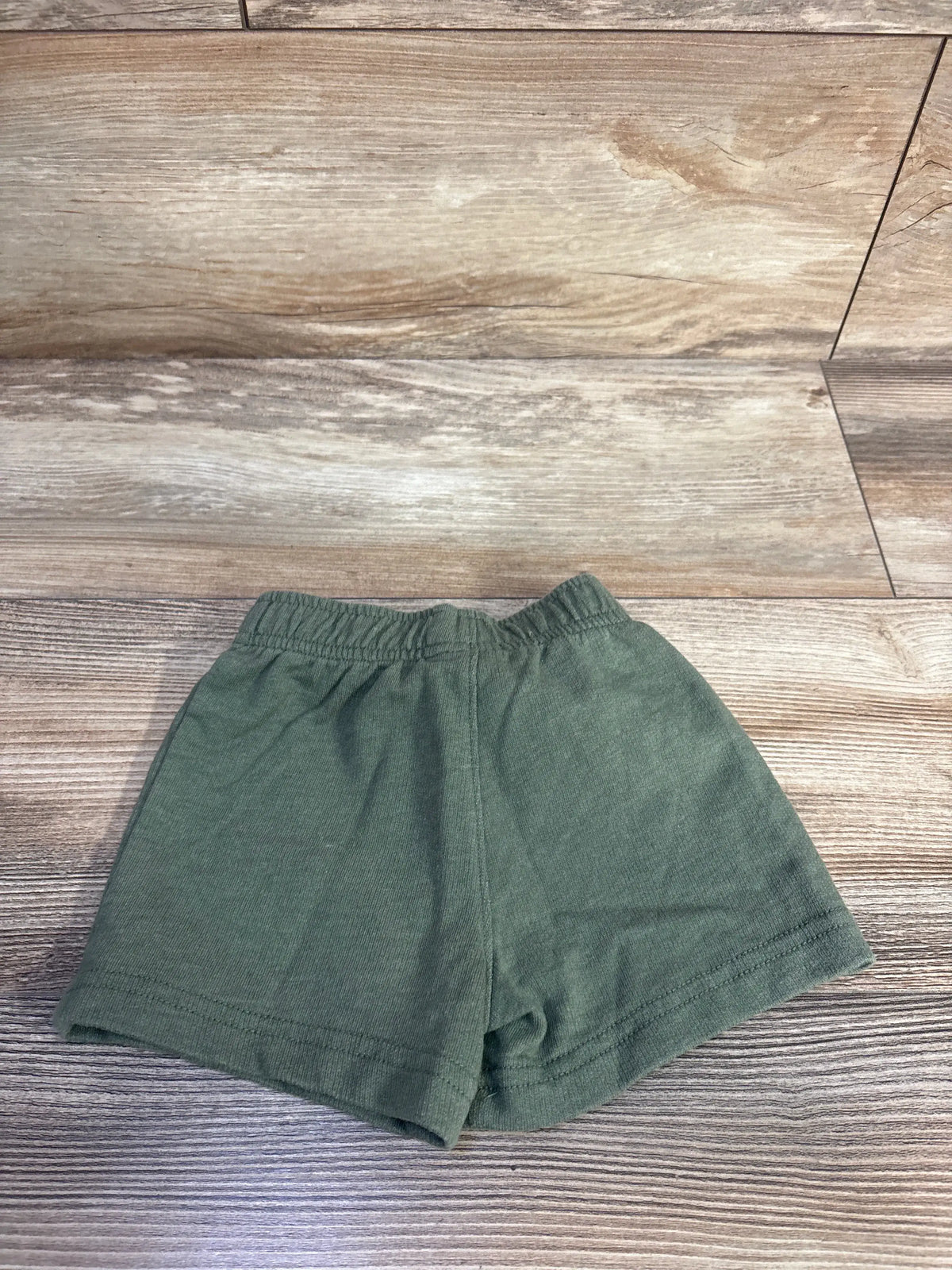 Front view of Carter’s green pull-on shorts size 12 months showcasing elastic waistband on a wood-patterned floor