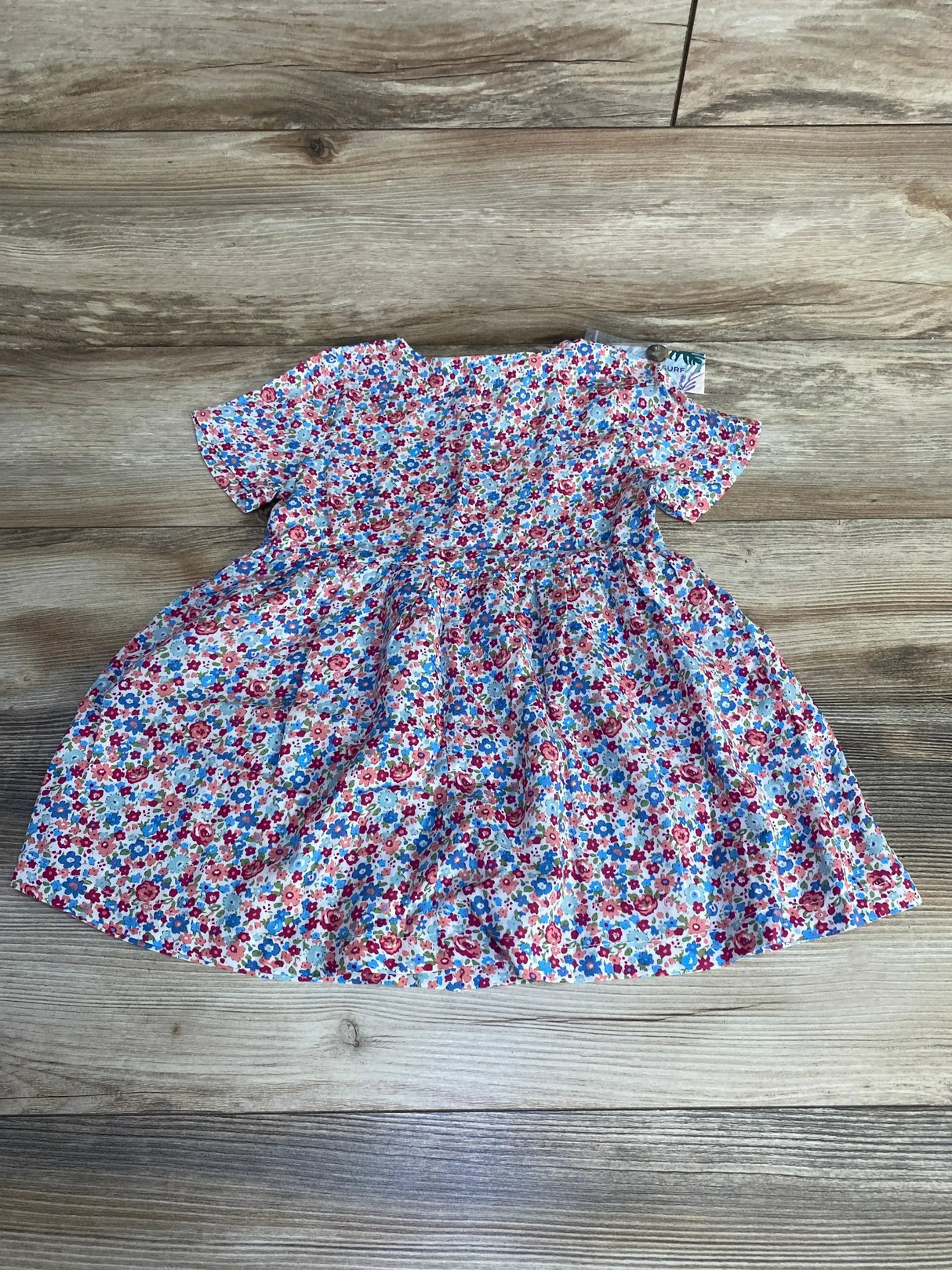 Flat-lay of multicolor Brass & Roe Ophelia toddler dress (size 2T) showing short sleeves and floral print on wood floor background