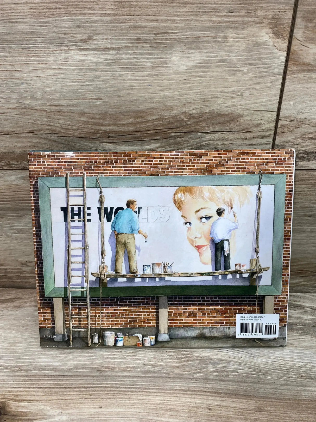 Back cover view of The Sign Painter hardcover book showcasing illustrated billboard artwork with wooden tabletop background