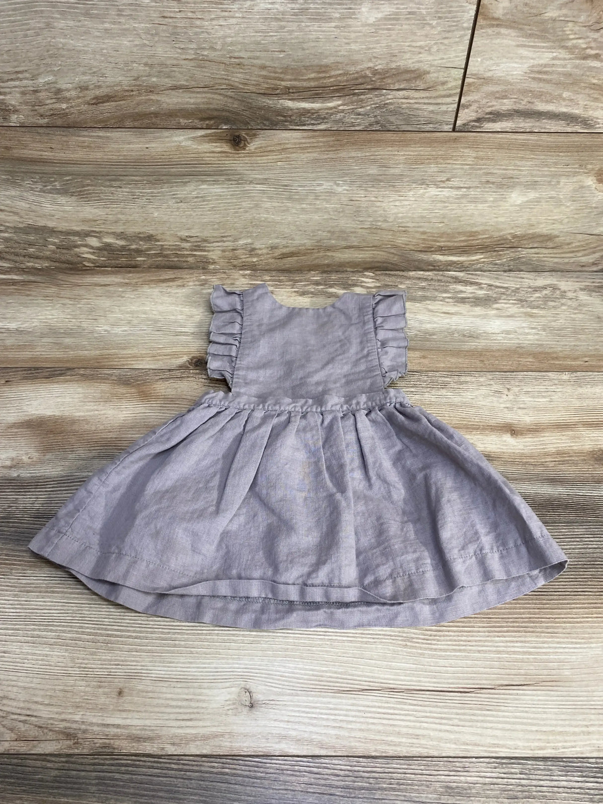 Flat lay of Beba Bean linen pinafore dress in grey showcasing ruffled cap sleeves and gathered skirt on wood background