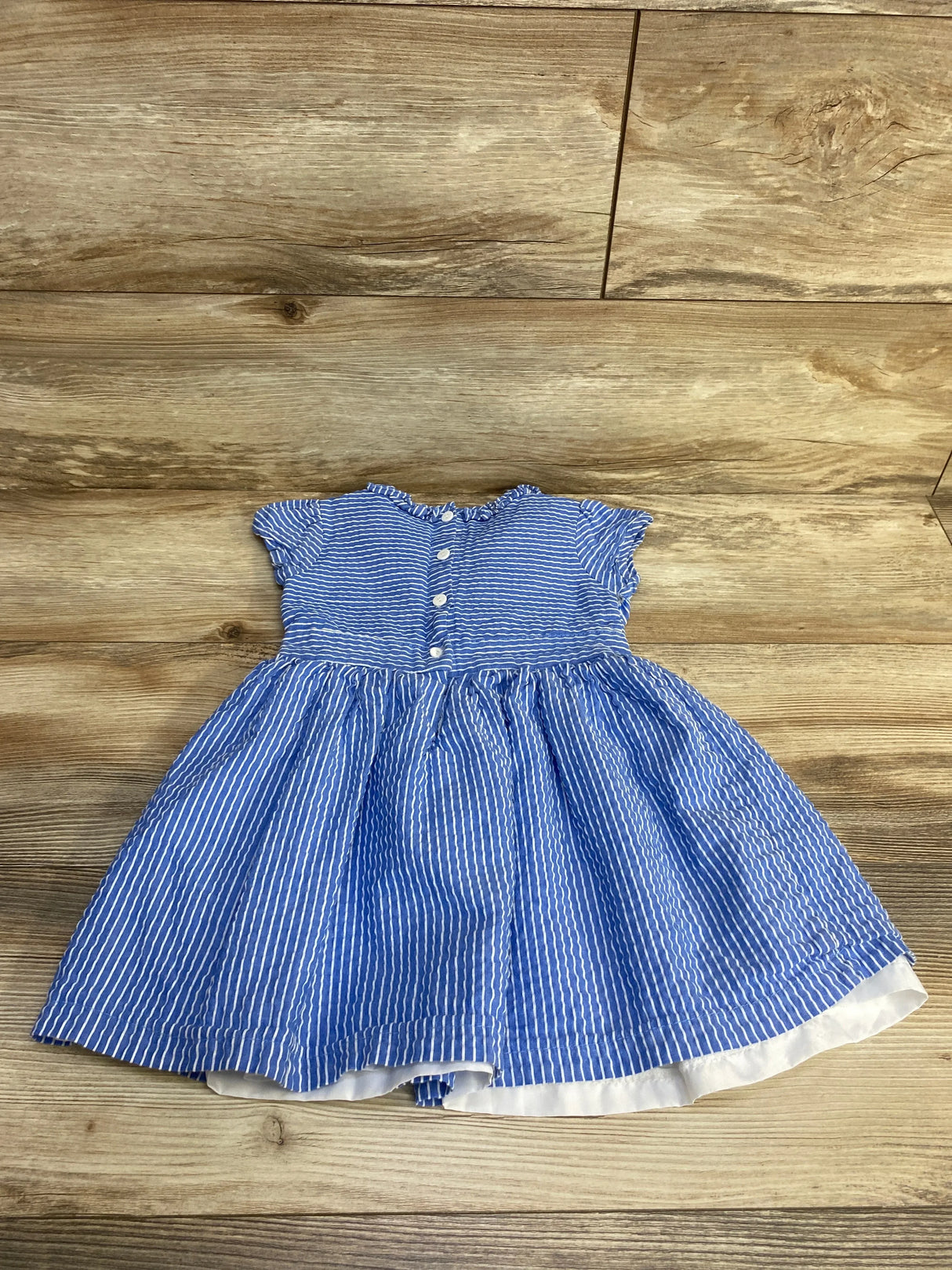 Flat lay blue striped seersucker toddler dress 3T with ruffled cap sleeves, button front and gathered skirt on wood background