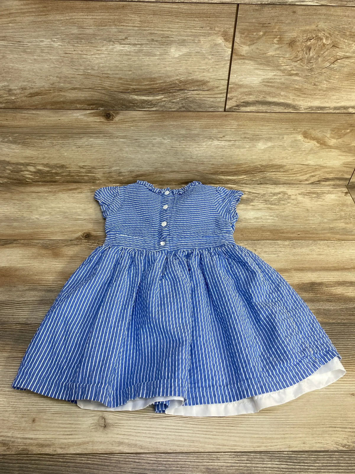 Flat lay blue striped seersucker toddler dress 3T with ruffled cap sleeves, button front and gathered skirt on wood background
