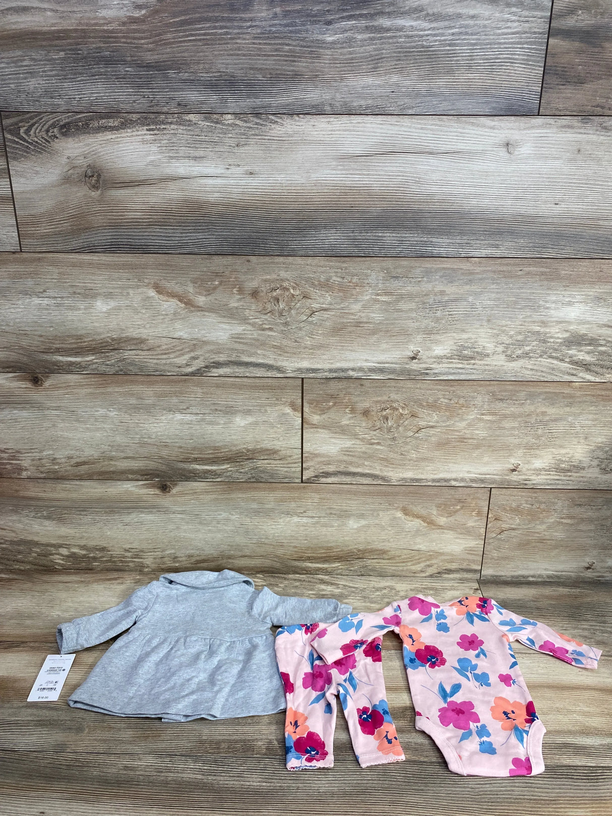 Baby girl clothing set with gray dress, floral bodysuit, and matching pants on wood floor