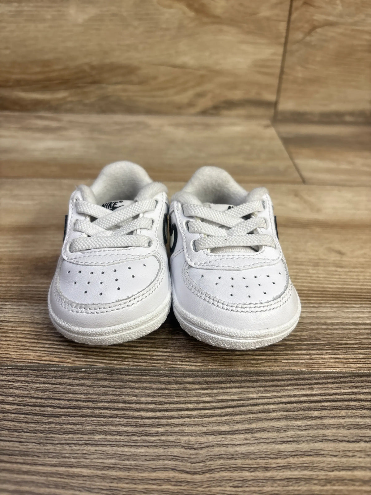 Front view of Nike Force 1 CB white and black sneakers showcasing laces and perforated toes on a wood surface