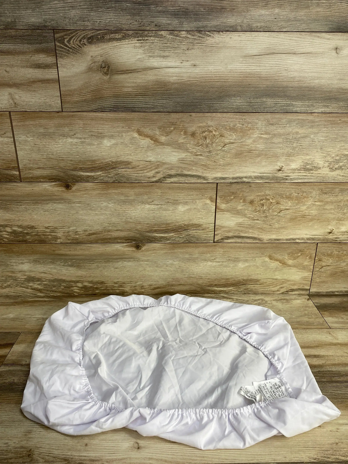 White fitted crib mattress sheet with elastic edges on wooden floor background