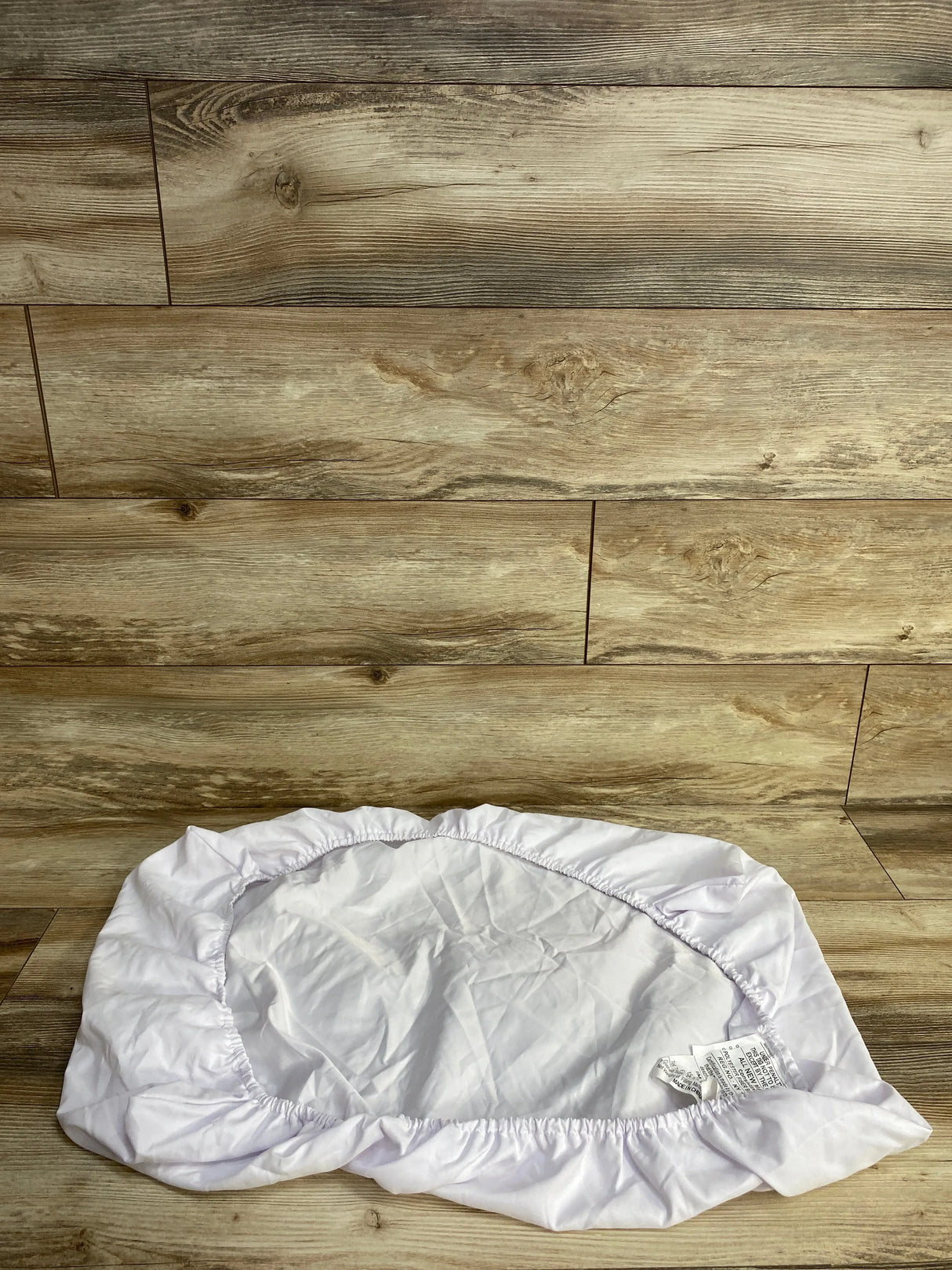 White fitted crib mattress sheet with elastic edges on wooden floor background